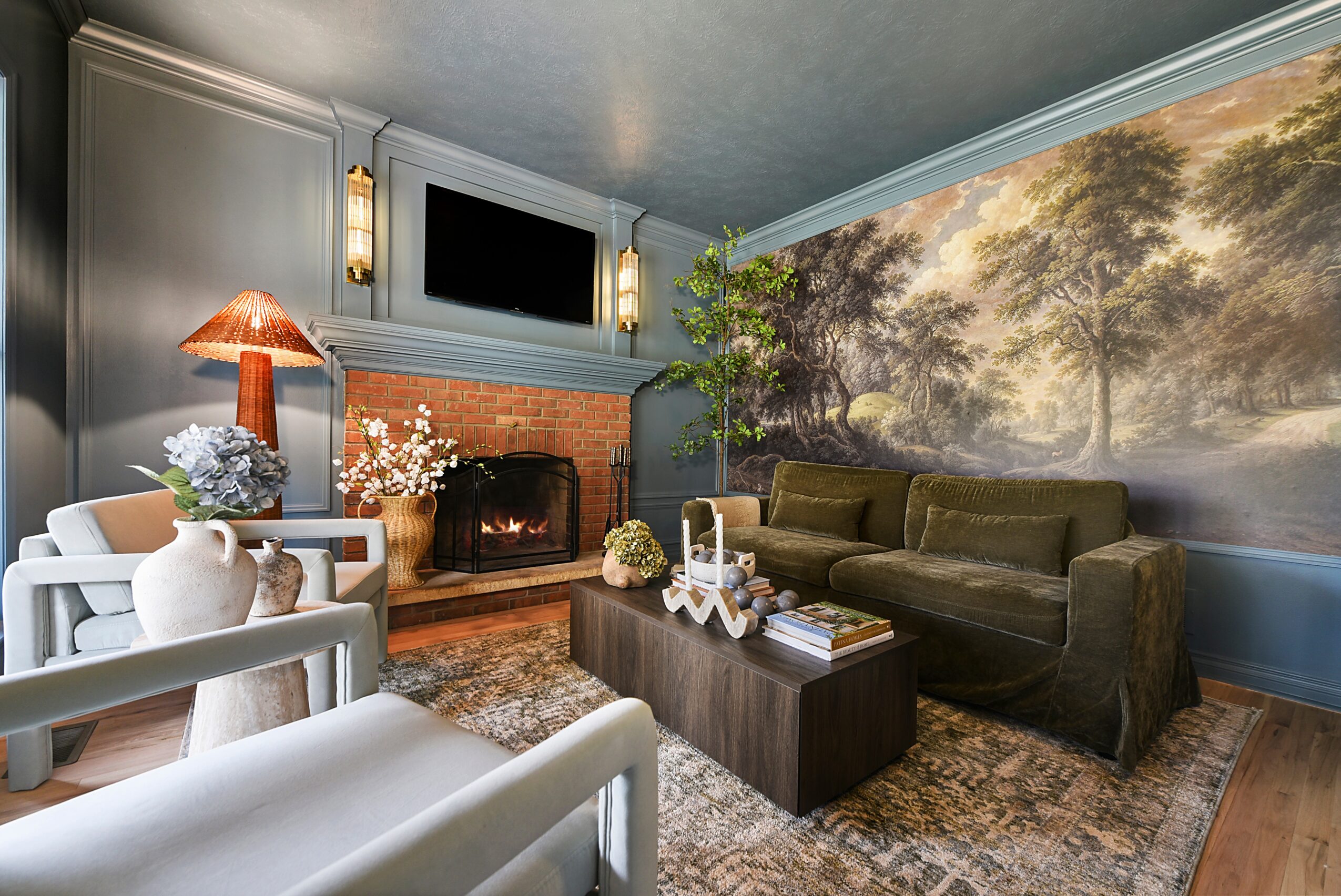 Living room with a green sofa, fireplace, wall mural of trees, and a coffee table with decorative items.