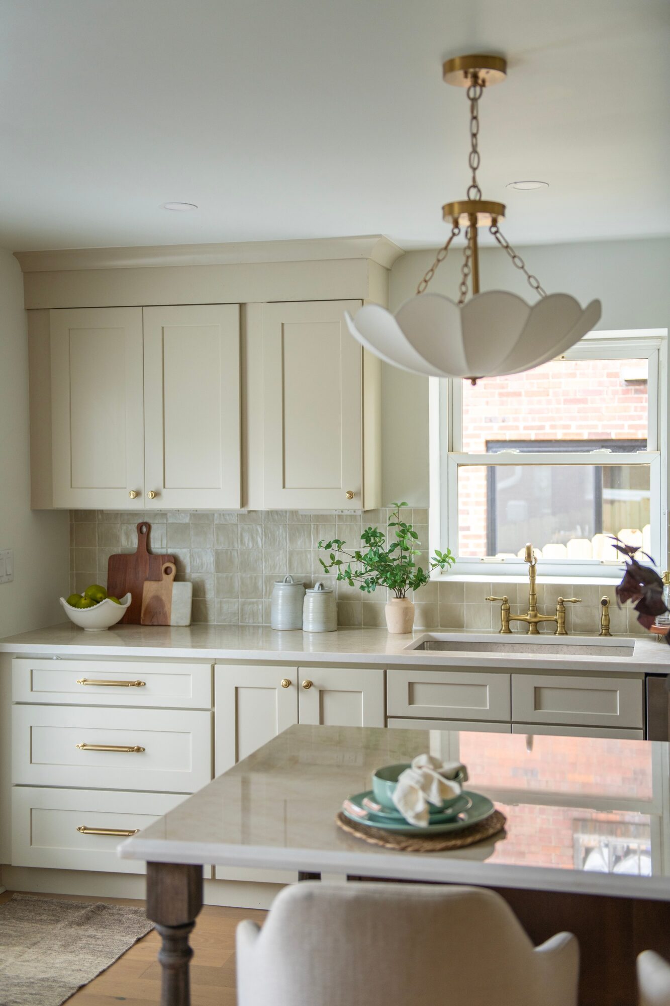 Kitchen with white cabinets, a window, a plant, and a hanging light fixture, with a countertop and a table in the foreground.