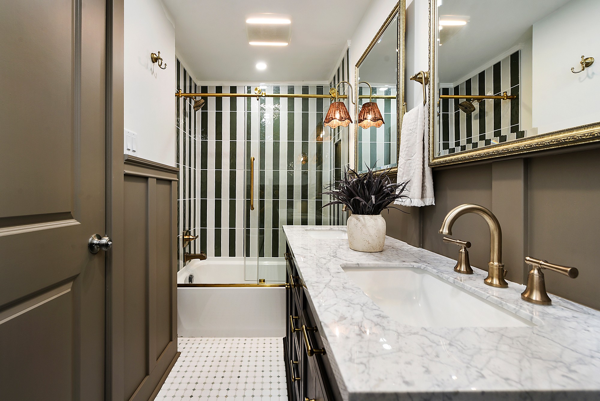 Bathroom with striped wall, marble countertop, gold fixtures, and large mirror, featuring a potted plant and towel. Word count: 20