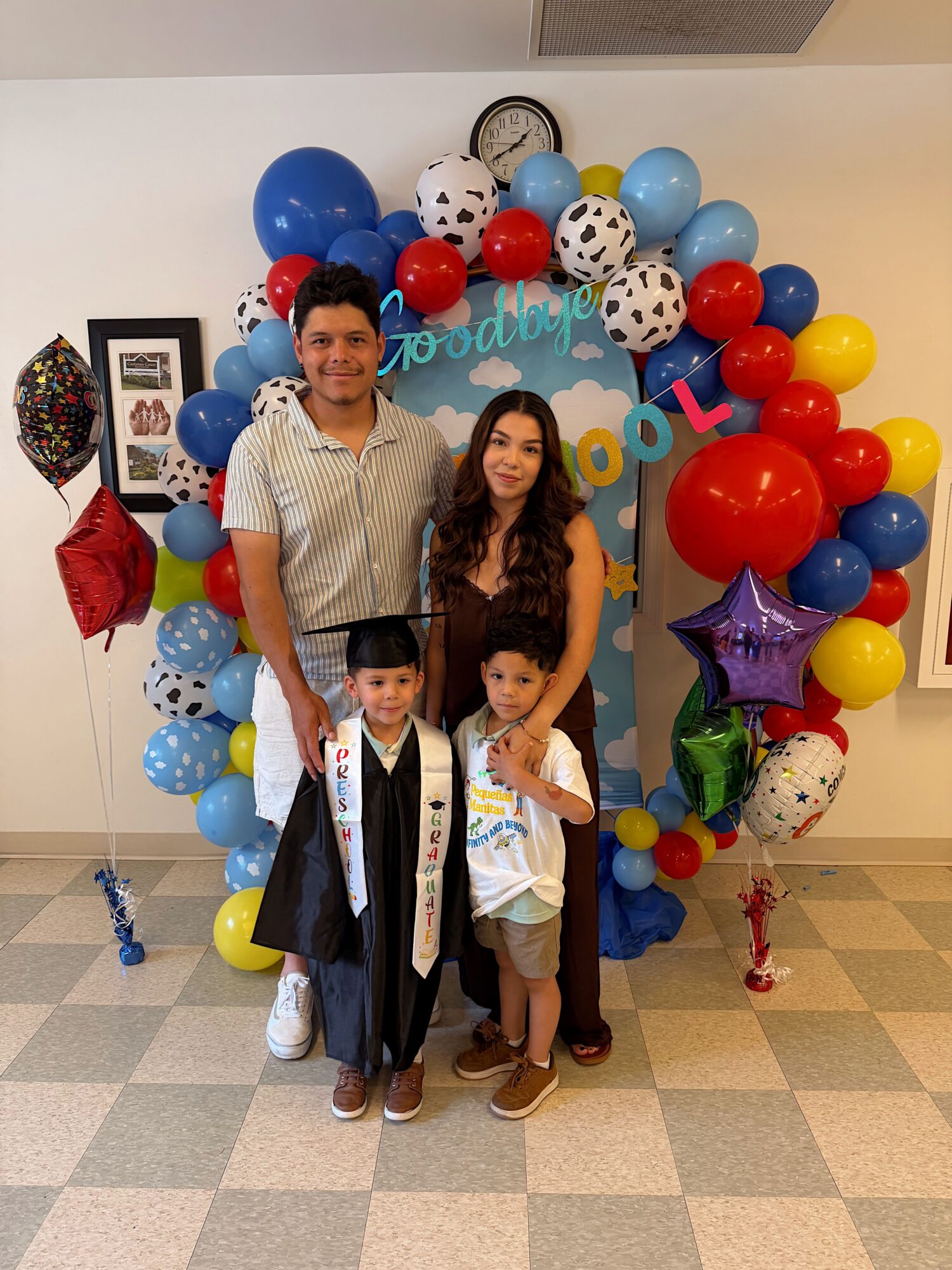 Three people standing in front of a colorful balloon arch at a celebration, with balloons and decorations around them.