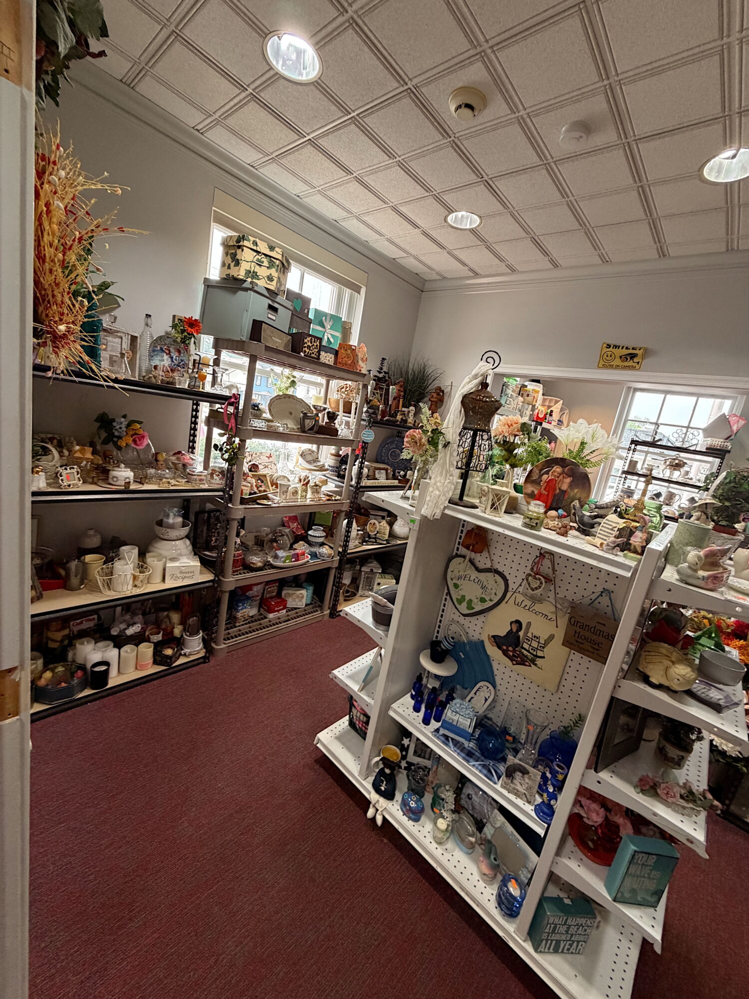 View of a store interior with shelves filled with various decorative items and collectibles, ceiling with grid pattern, and windows letting in natural light.