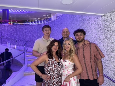 Group of five people smiling indoors with purple lighting and curved staircase in background.