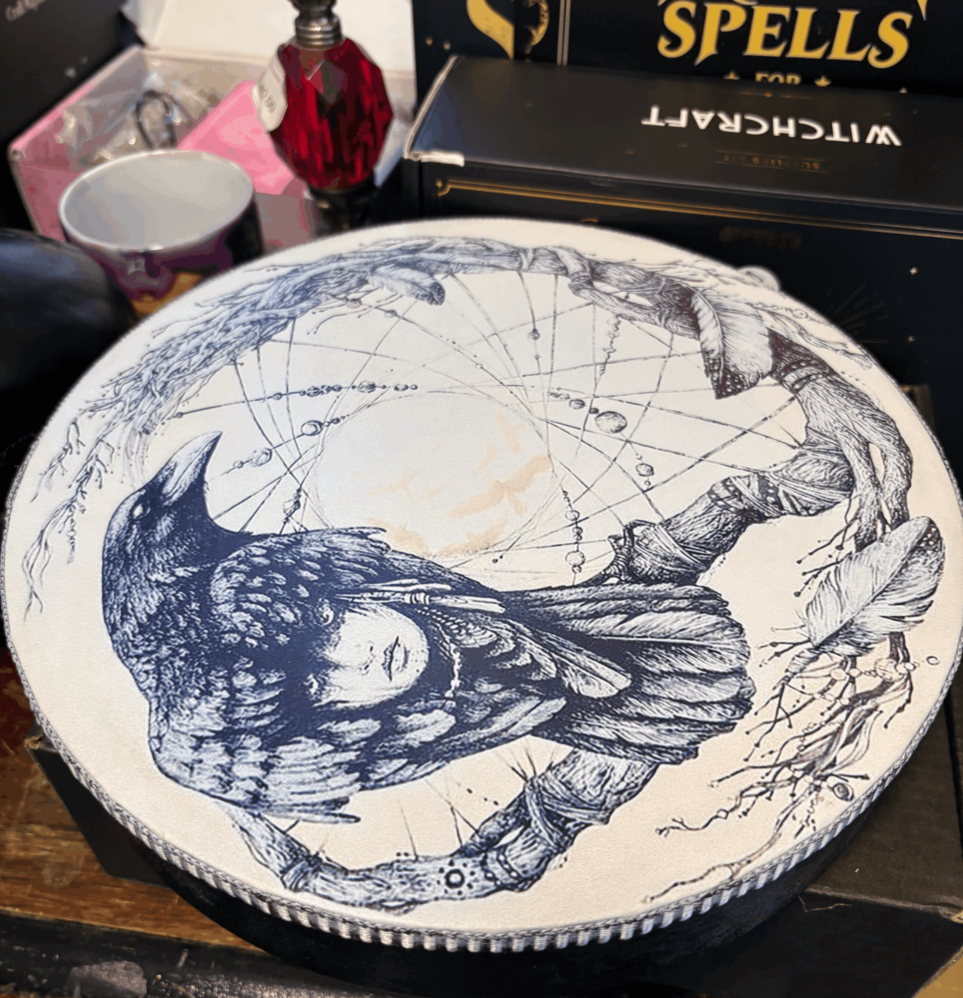 Decorative round object with a detailed illustration of a woman with long hair, surrounded by a map-like background, on a cluttered surface.