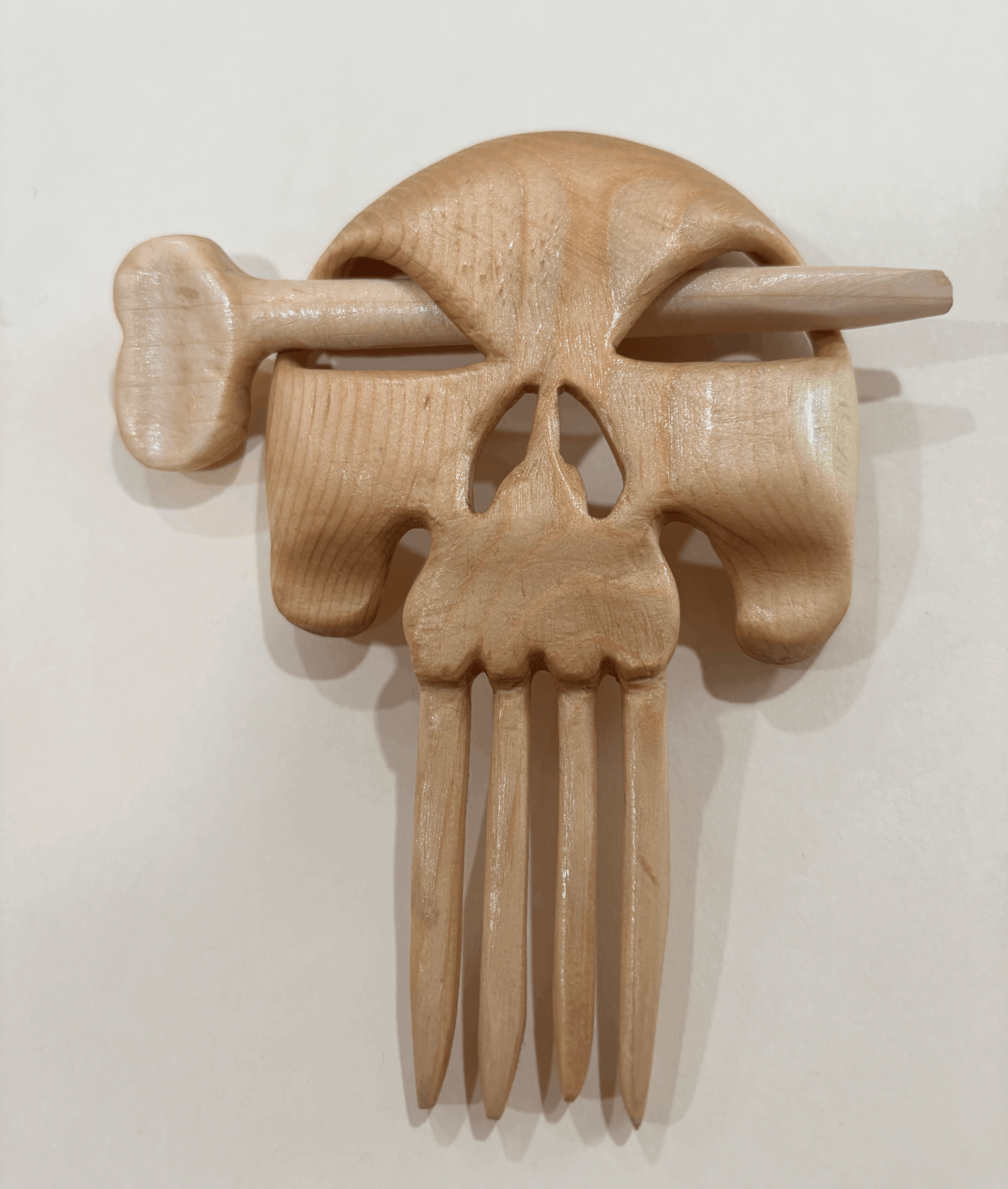 Wooden wall decoration resembling a face with a bone through it, featuring carved details and a fork at the bottom.
