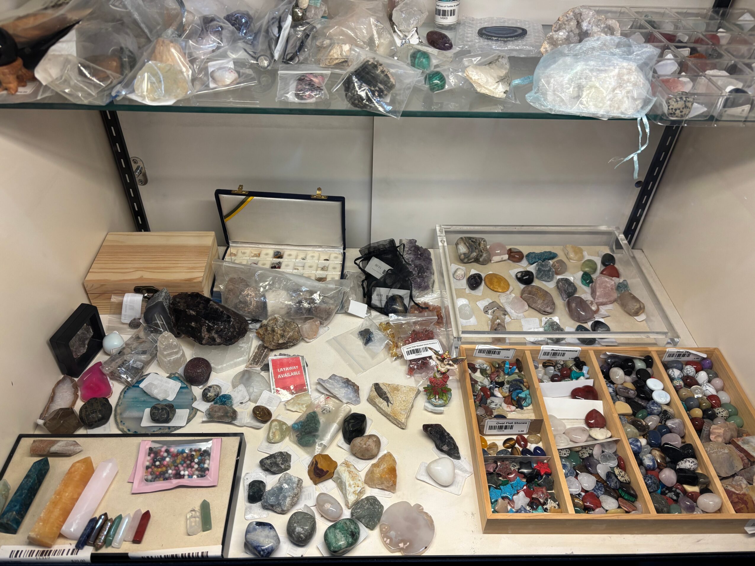Display of various stones, crystals, and jewelry supplies on a table with organized boxes and loose items.