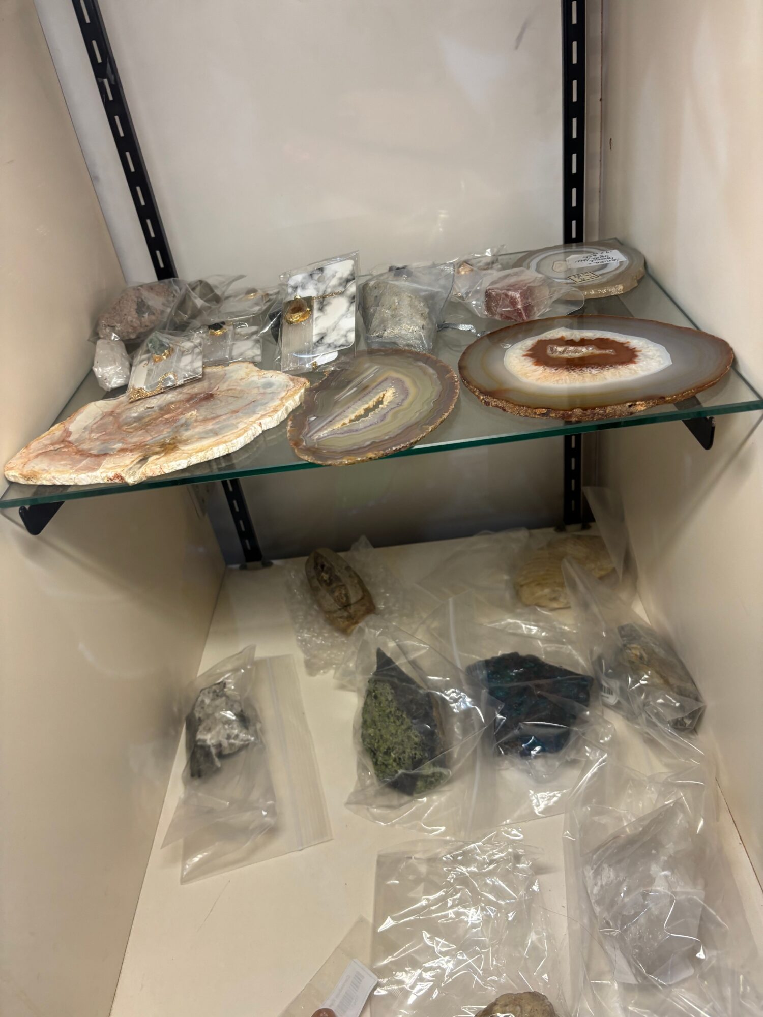 Stacked geodes and mineral specimens on a glass shelf, with plastic bags containing rocks nearby.