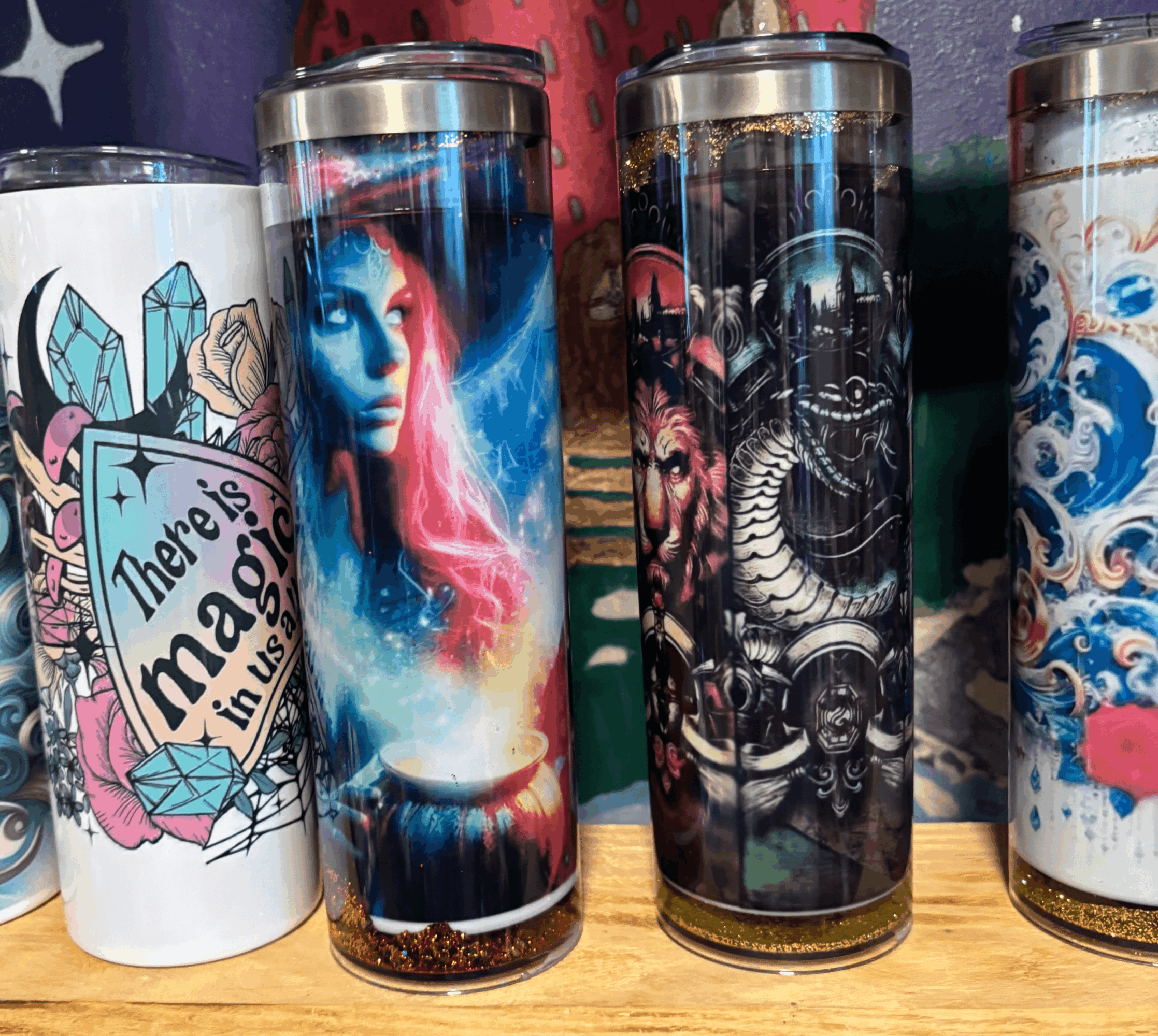 Four tall tumblers with colorful designs, including a girl with blue hair, a dragon, and abstract patterns, on a wooden surface.