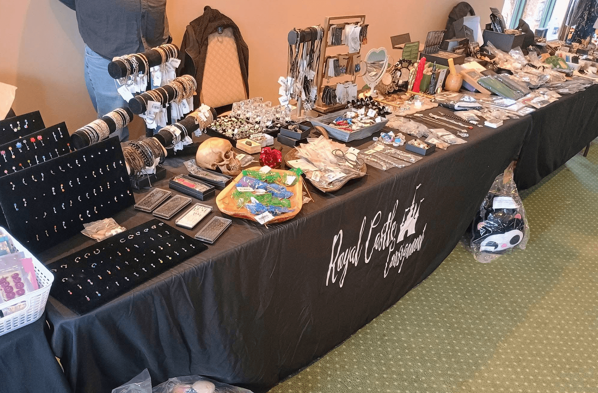 Table with jewelry, accessories, and small items displayed for sale, covered with a black cloth, in a room with green carpet.