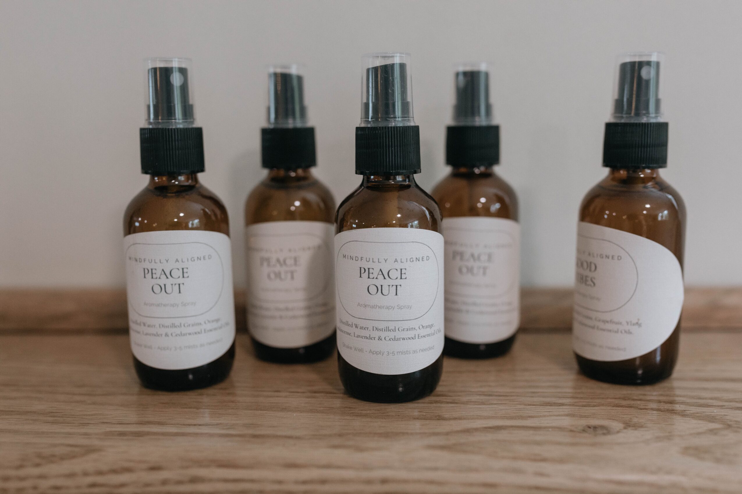 Five small brown spray bottles with black caps and white labels arranged on a wooden surface.