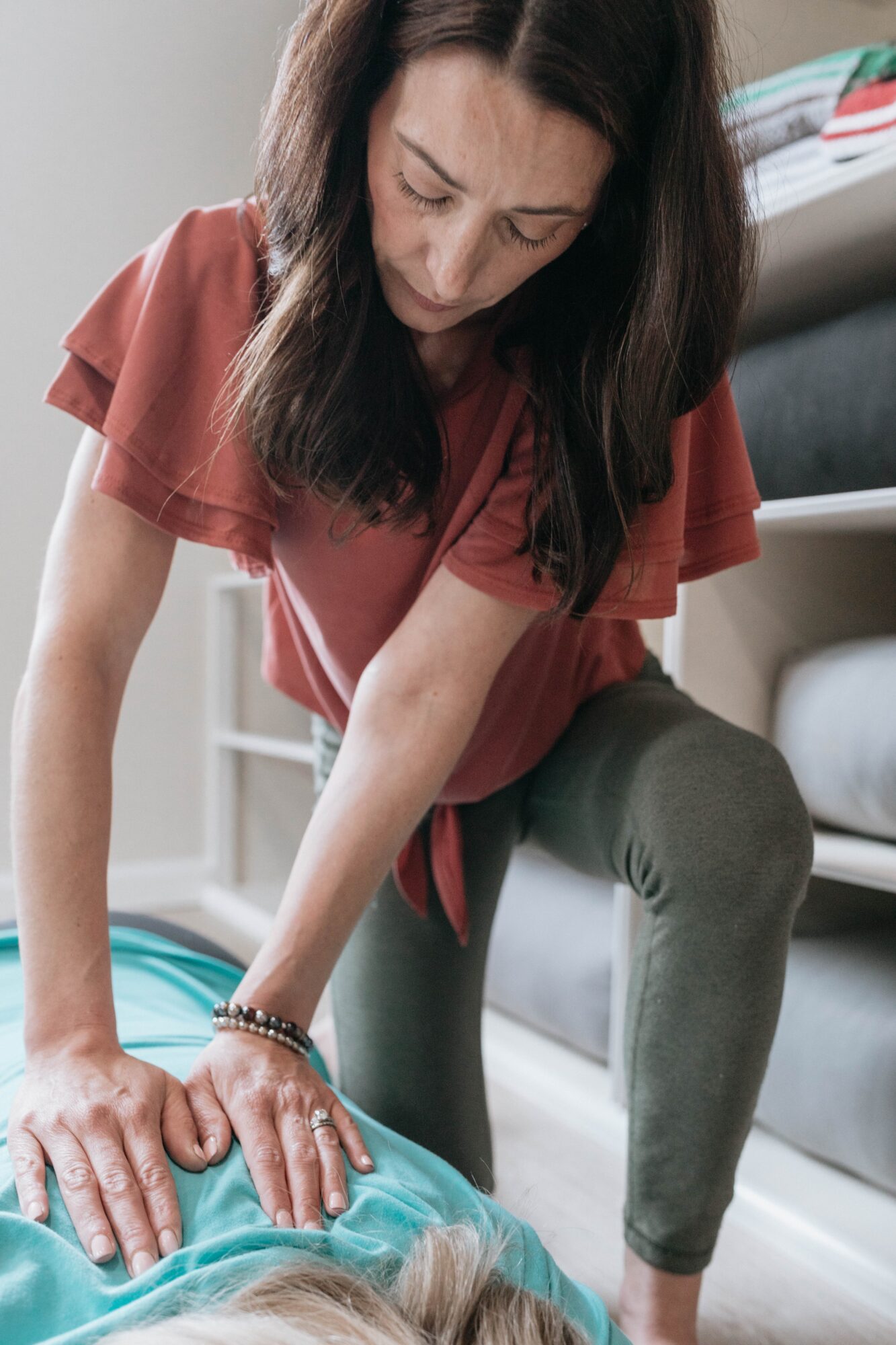 Woman leaning over a person lying on a bed, performing CPR, in a bedroom setting.