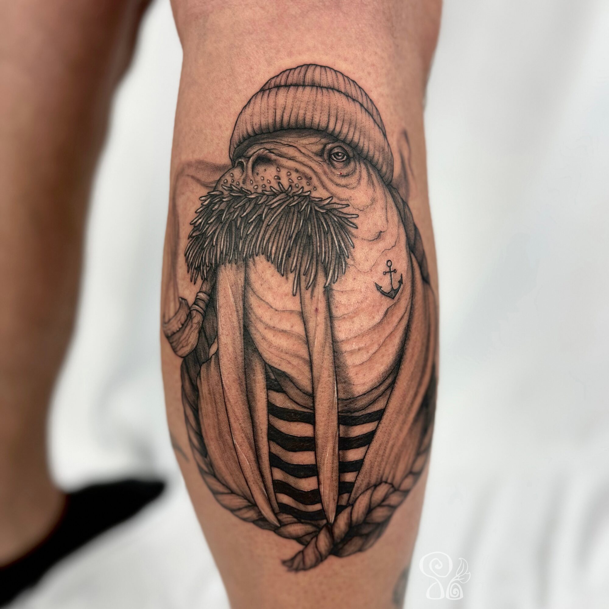 Tattoo of a bearded man with a beanie, striped shirt, and an anchor, inside a circular frame.