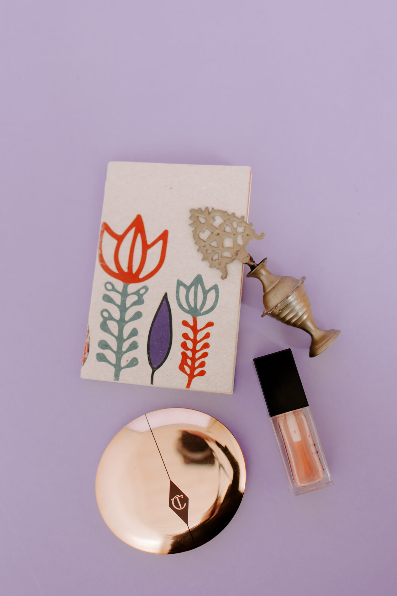 Decorative card with floral illustrations, a small seashell, a lipstick, and a round mirror on a purple background.