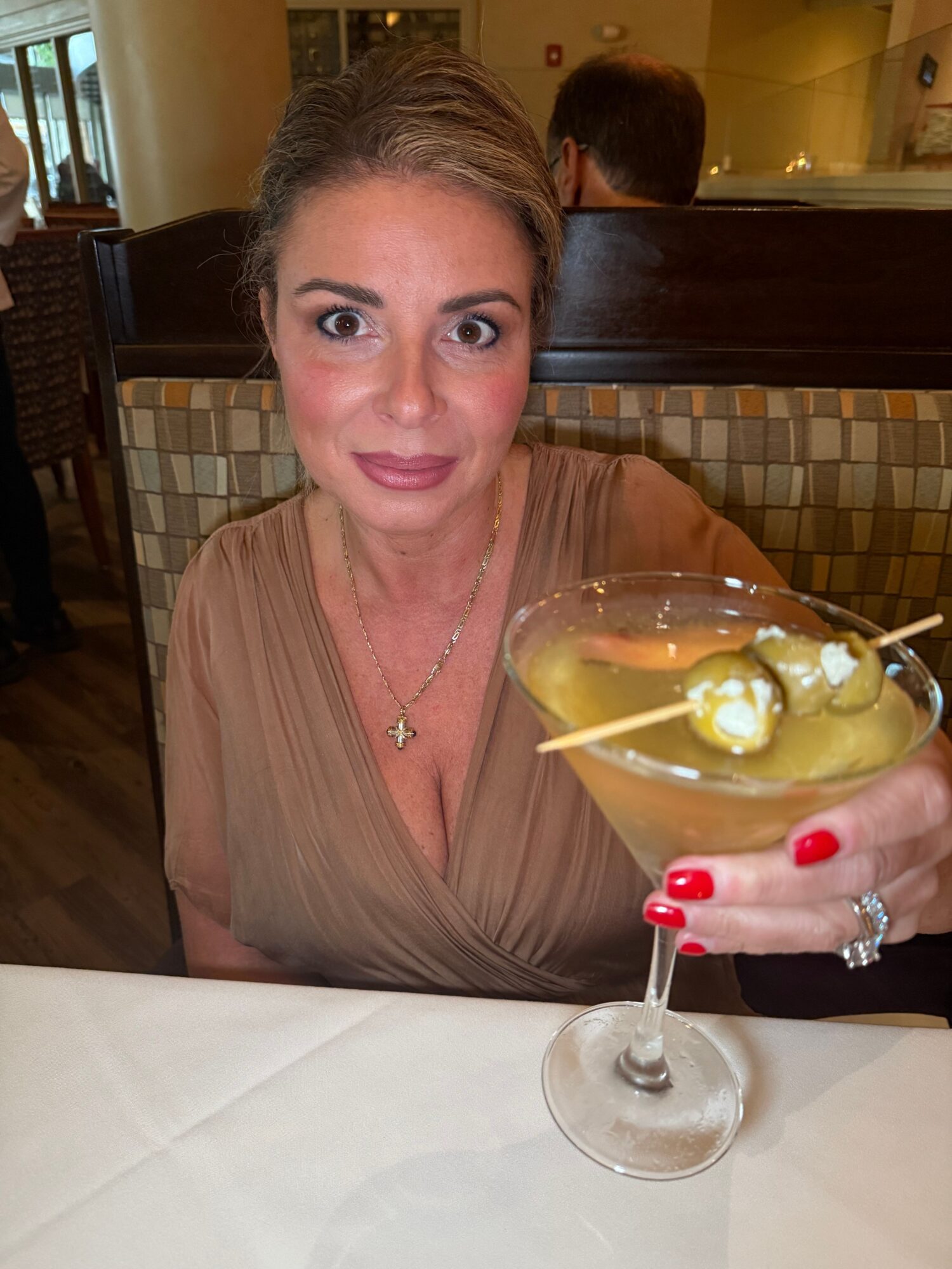 Woman with blonde hair and red lipstick holding a cocktail with lemon slices, sitting at a table in a restaurant.