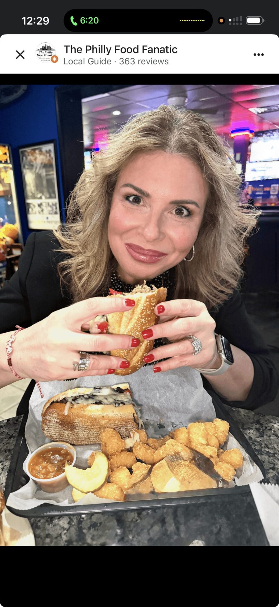 Woman with blonde hair holding a sandwich, surrounded by fried food on a tray, in a restaurant setting.