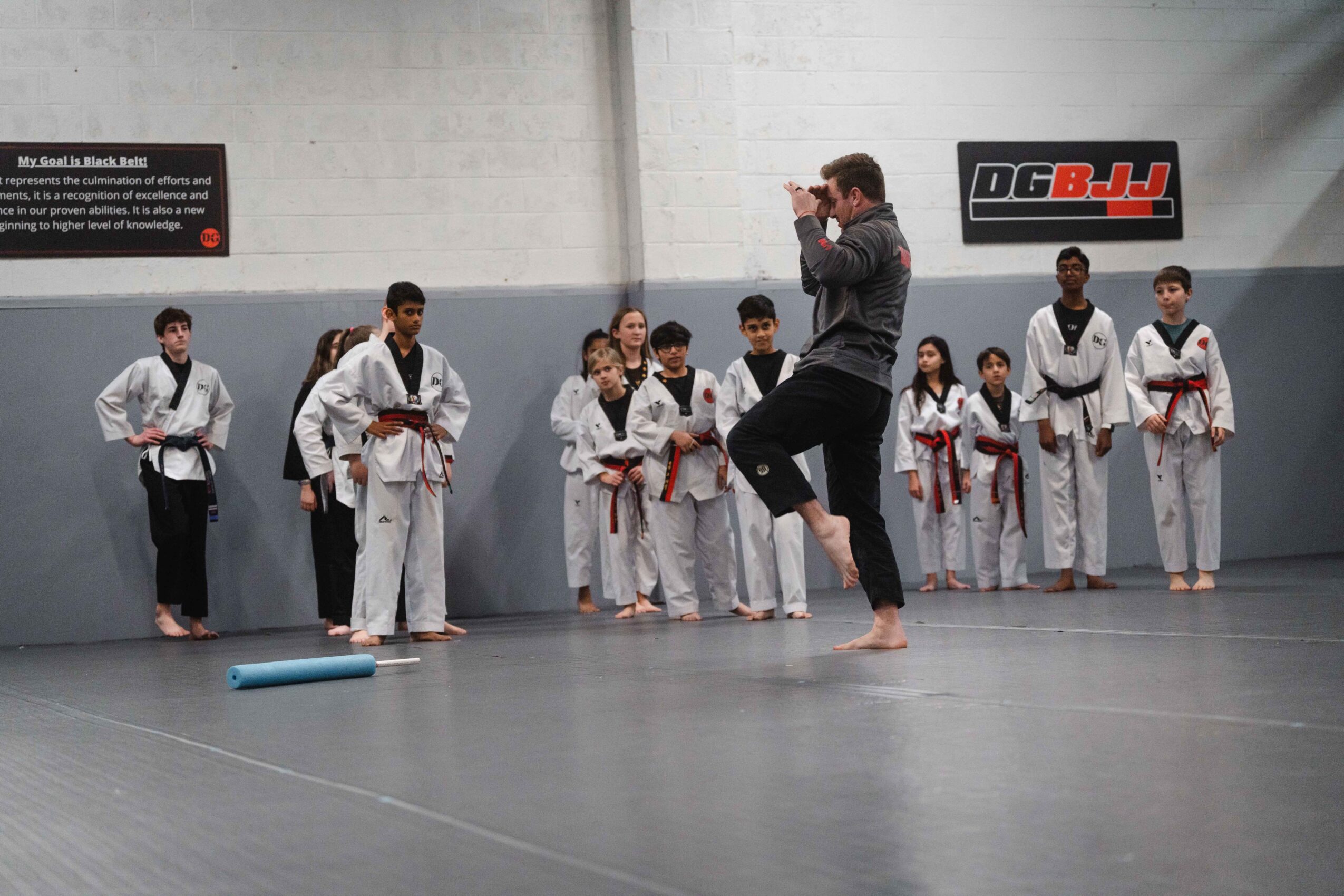 Martial arts class with children in white uniforms and a coach demonstrating techniques in a gym.