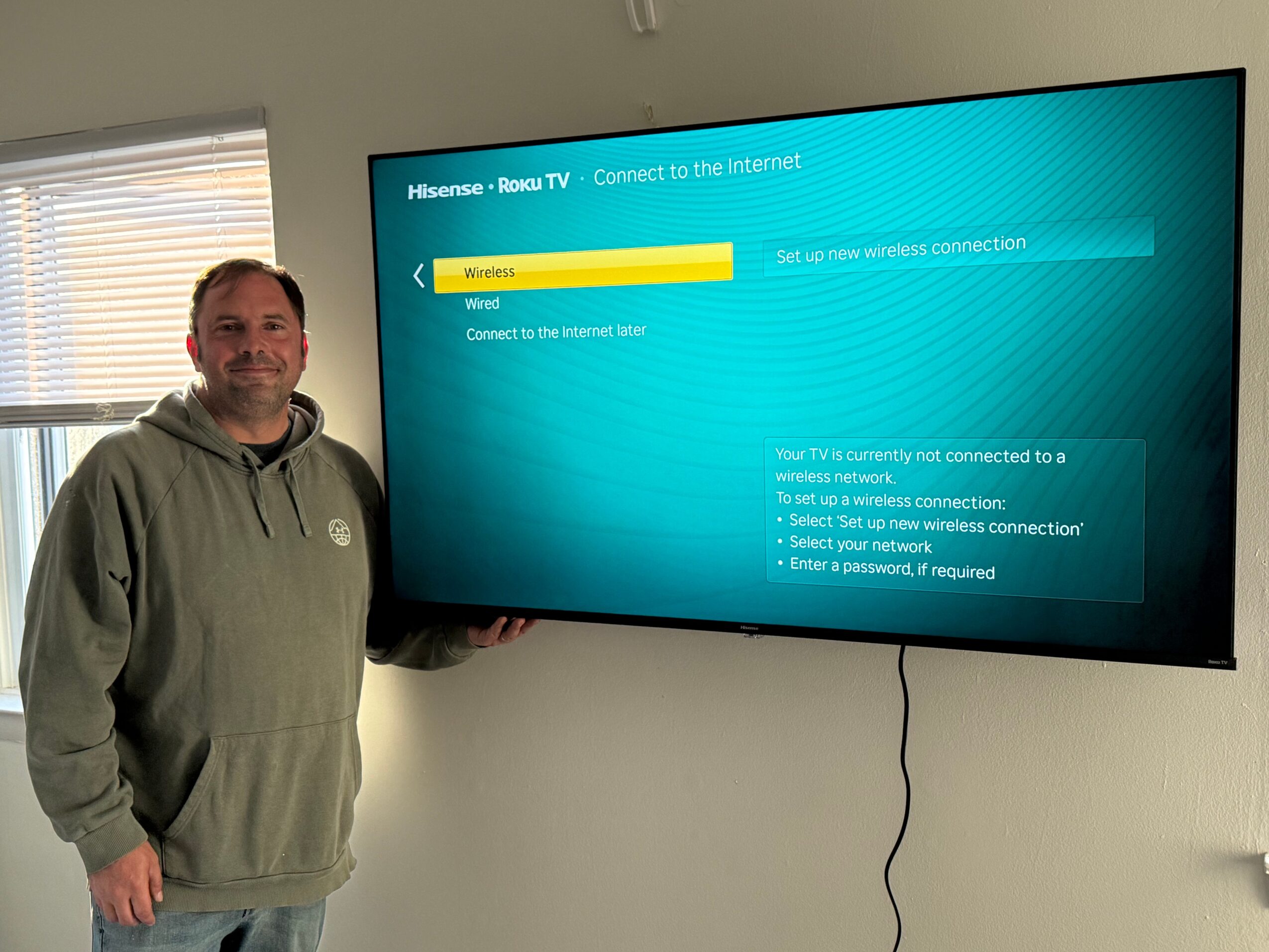Man standing next to a large flat-screen TV displaying a Wi-Fi connection error message.