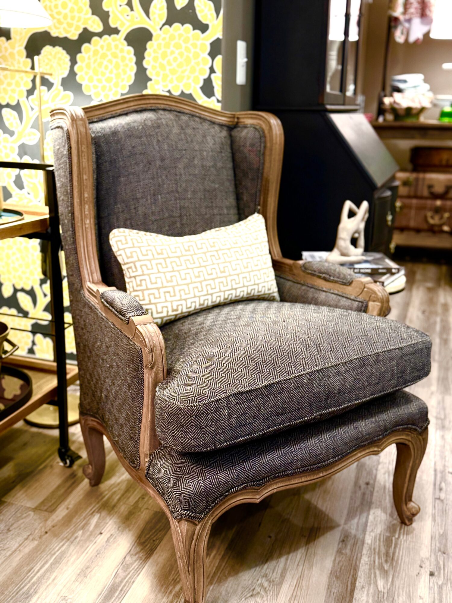 Upholstered armchair with wooden frame and a rectangular pillow, placed on a wooden floor in a room with decorative wall paneling.