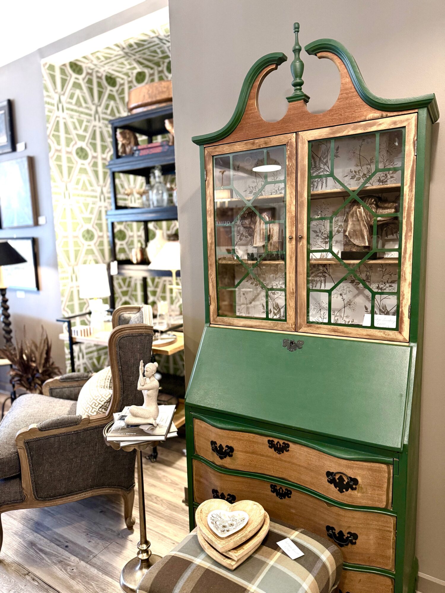 Green and wood display cabinet with glass doors and drawers, in a room with patterned wall and furniture.