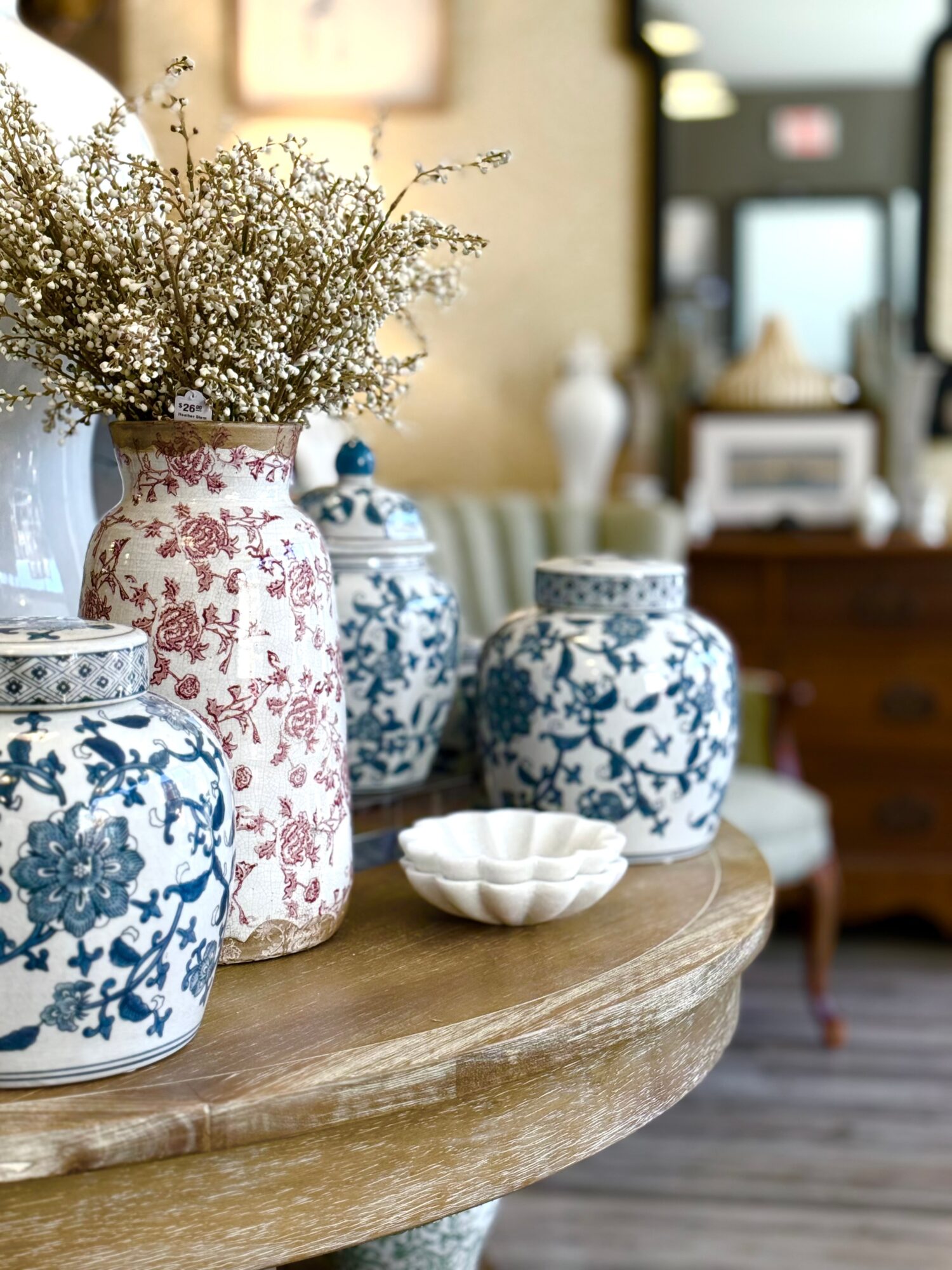 Vase with white flowers and blue and white patterned jars on a wooden table in a cozy room.
