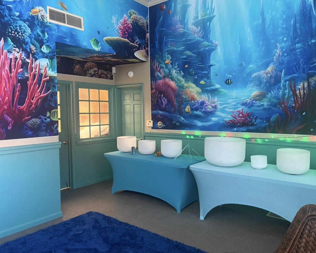 Room with ocean-themed mural, tables with white bowls, and a door with glass panes, decorated in blue tones.