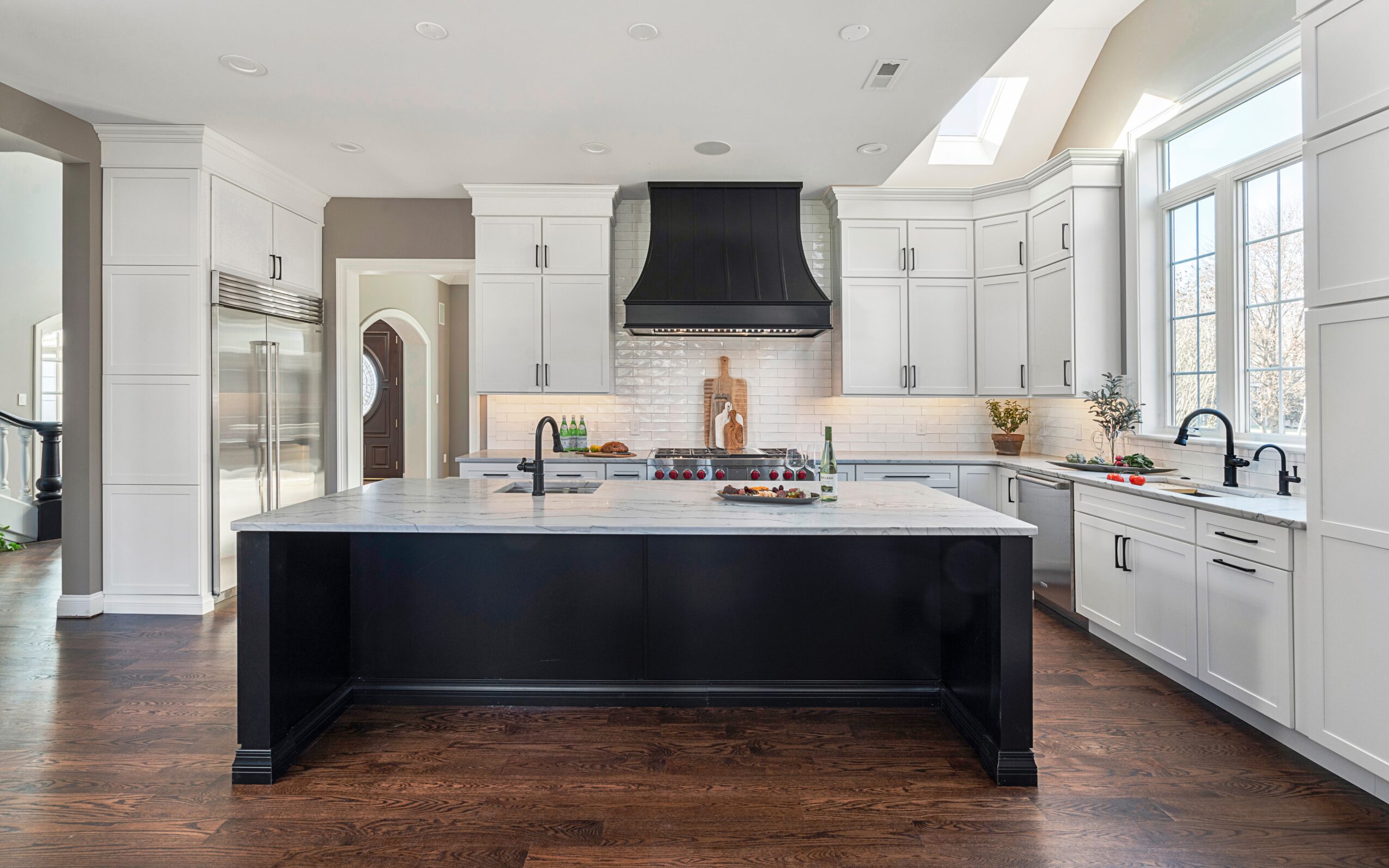 Modern kitchen with white cabinets, black island, large windows, and hardwood floors.