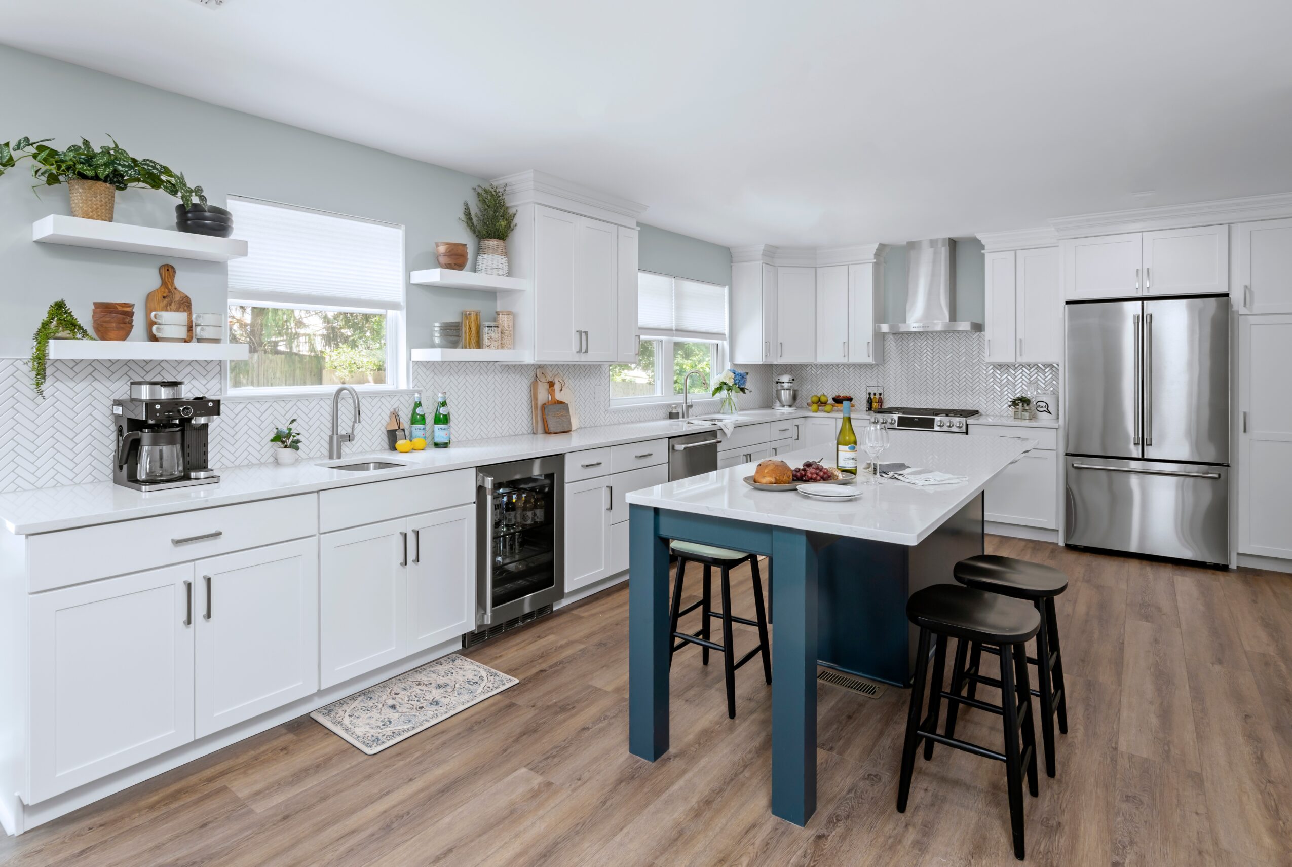 Modern kitchen with white cabinets, a central island with blue base, stainless steel appliances, and wooden flooring.