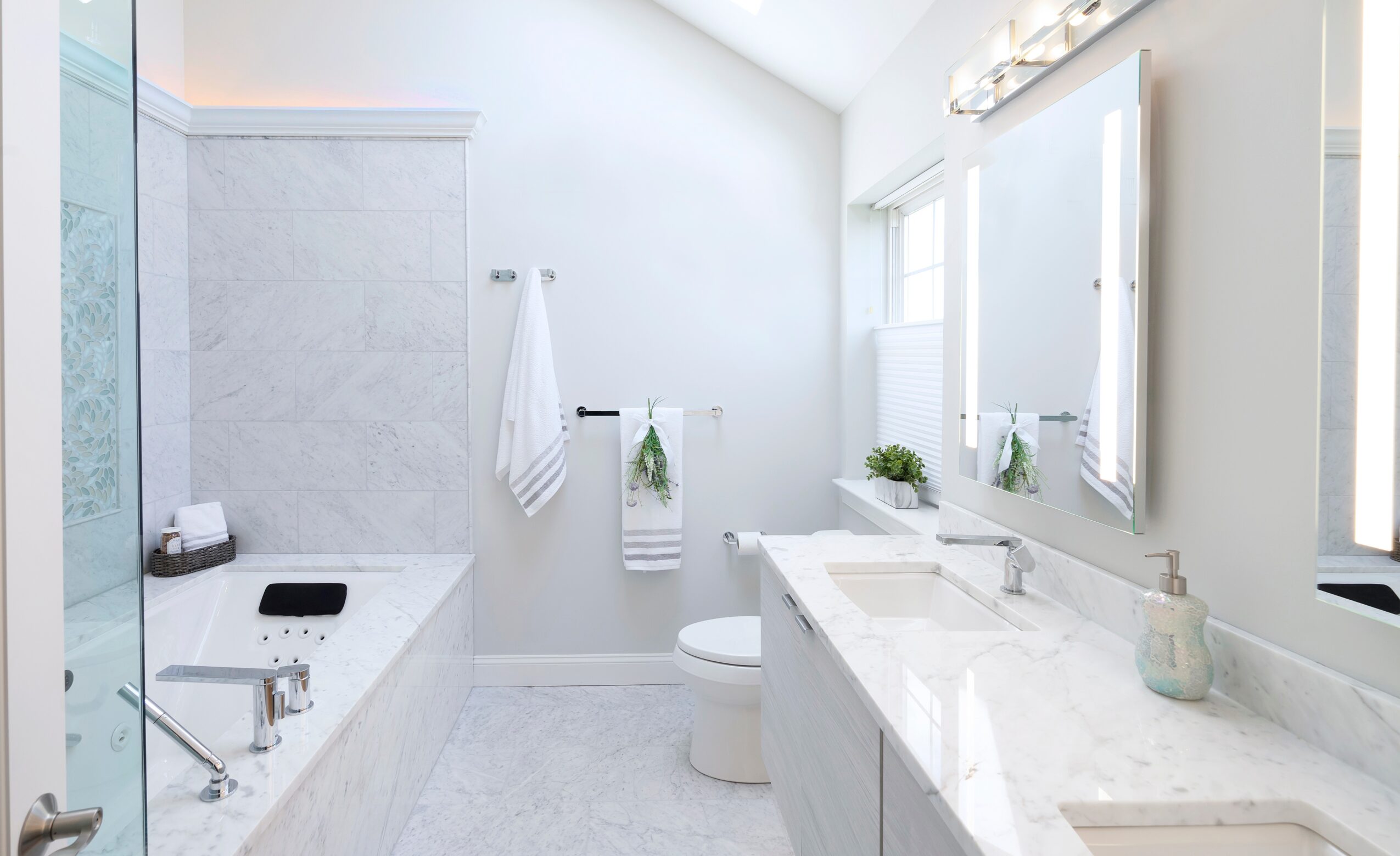 Bright bathroom with white walls, bathtub, toilet, and a large mirror above the sink, with natural light from windows.