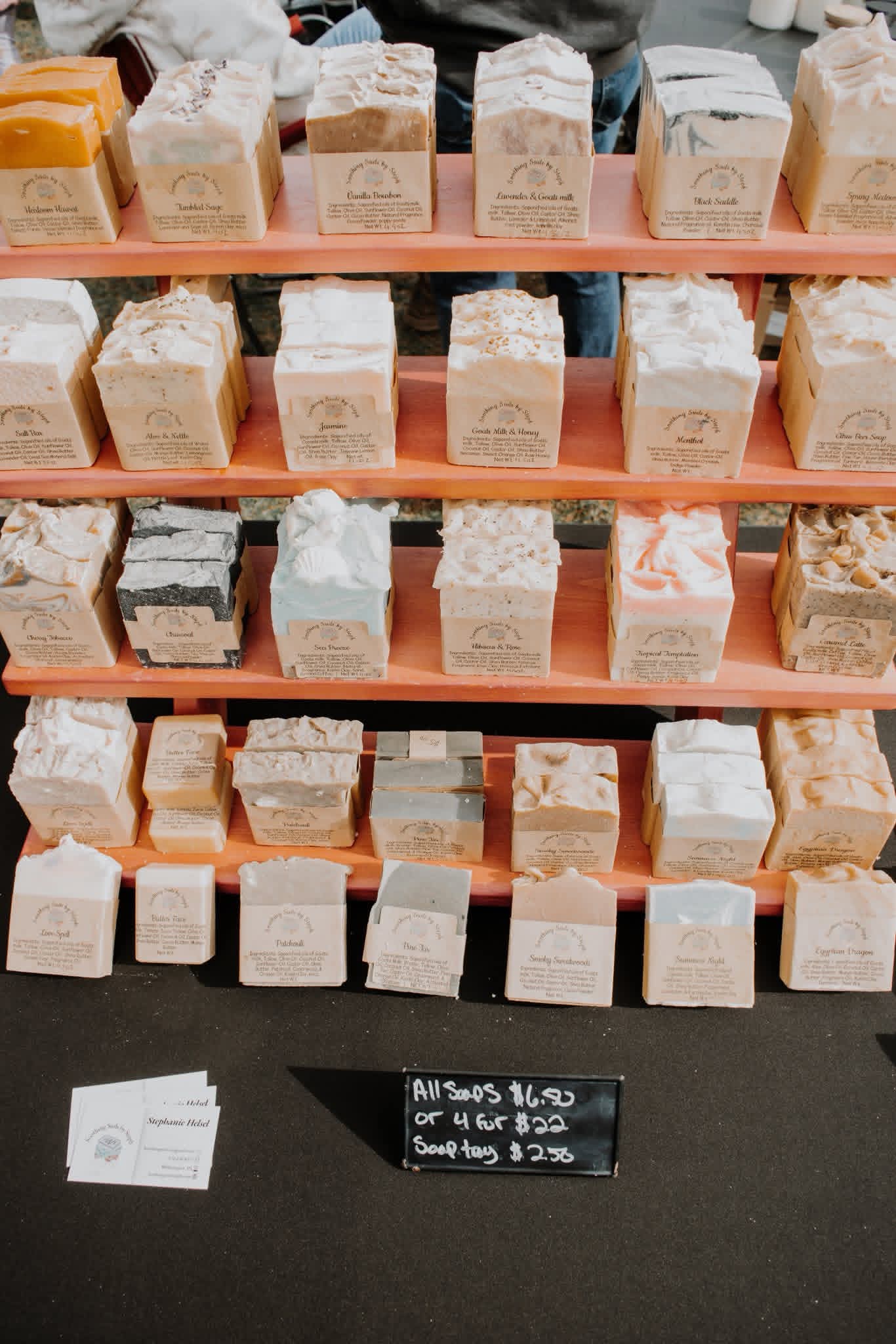 Display of various soap bars on shelves with a blackboard listing prices below.