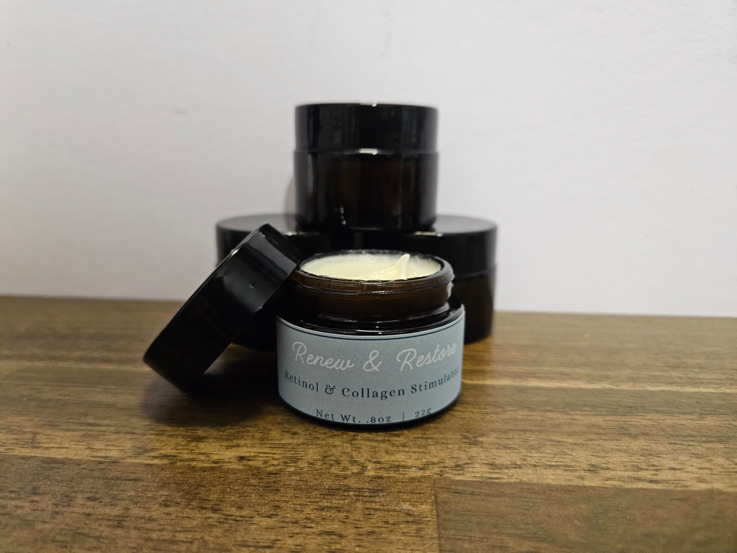 Open jar of cream or gel with black lid on wooden surface, with two closed jars behind it.