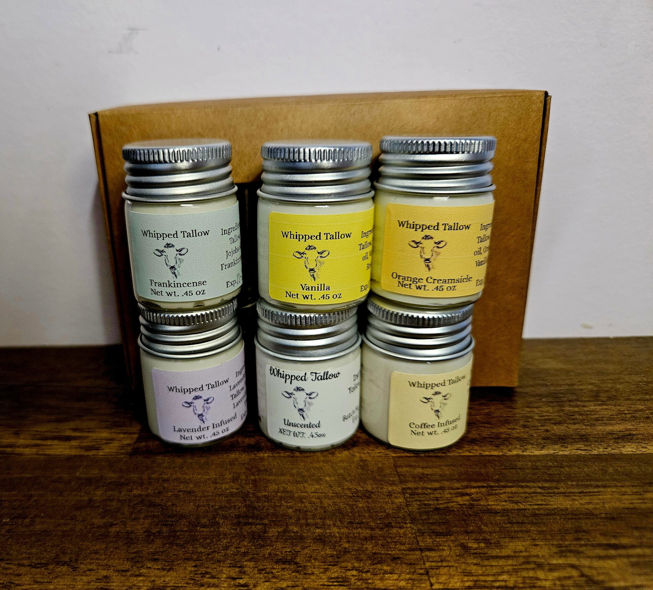 Six small jars with silver lids arranged on a wooden surface, with a wooden backrest behind them.