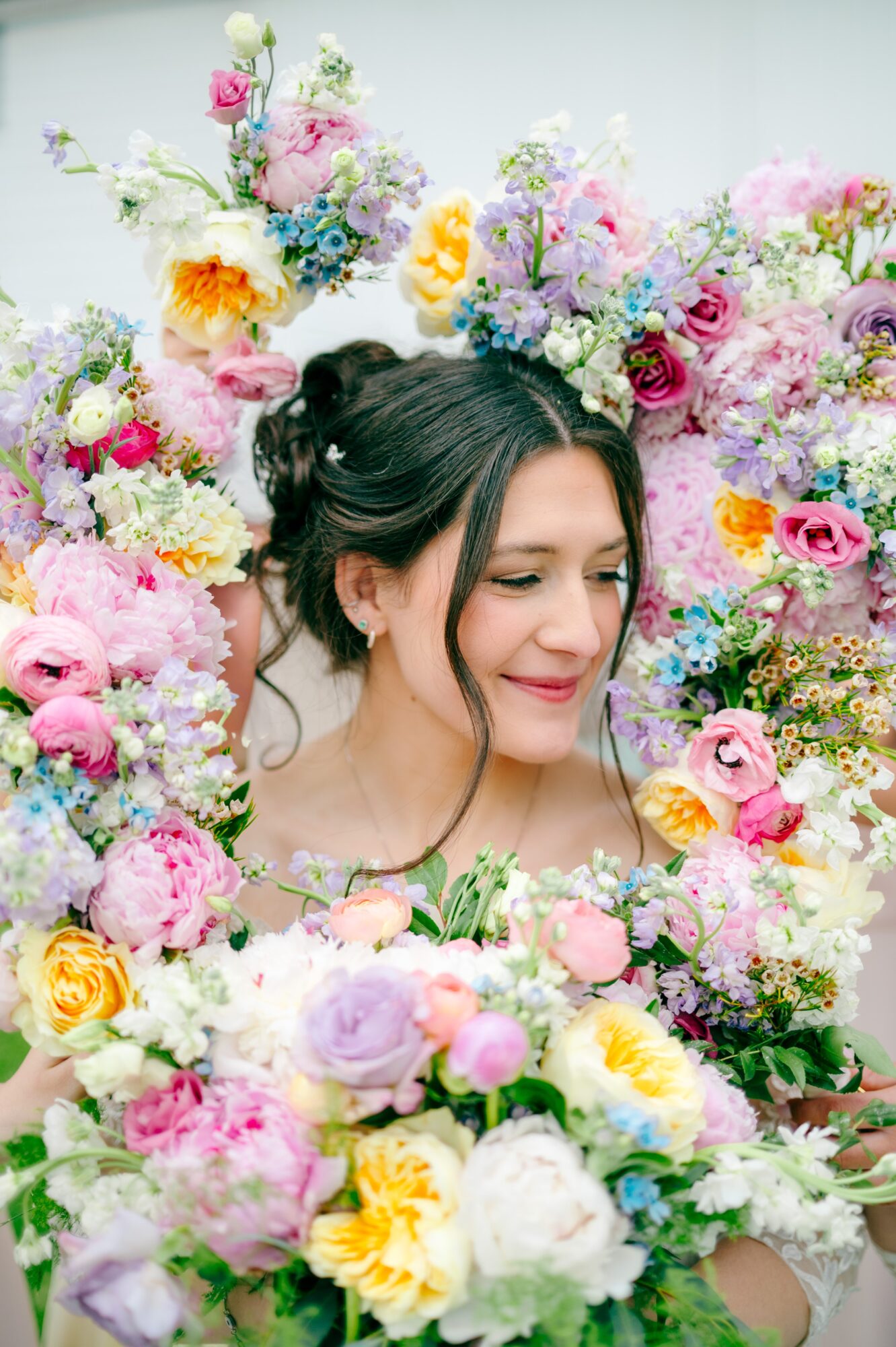 Young woman with dark hair in a floral setting, surrounded by colorful flowers, smiling gently with eyes closed.