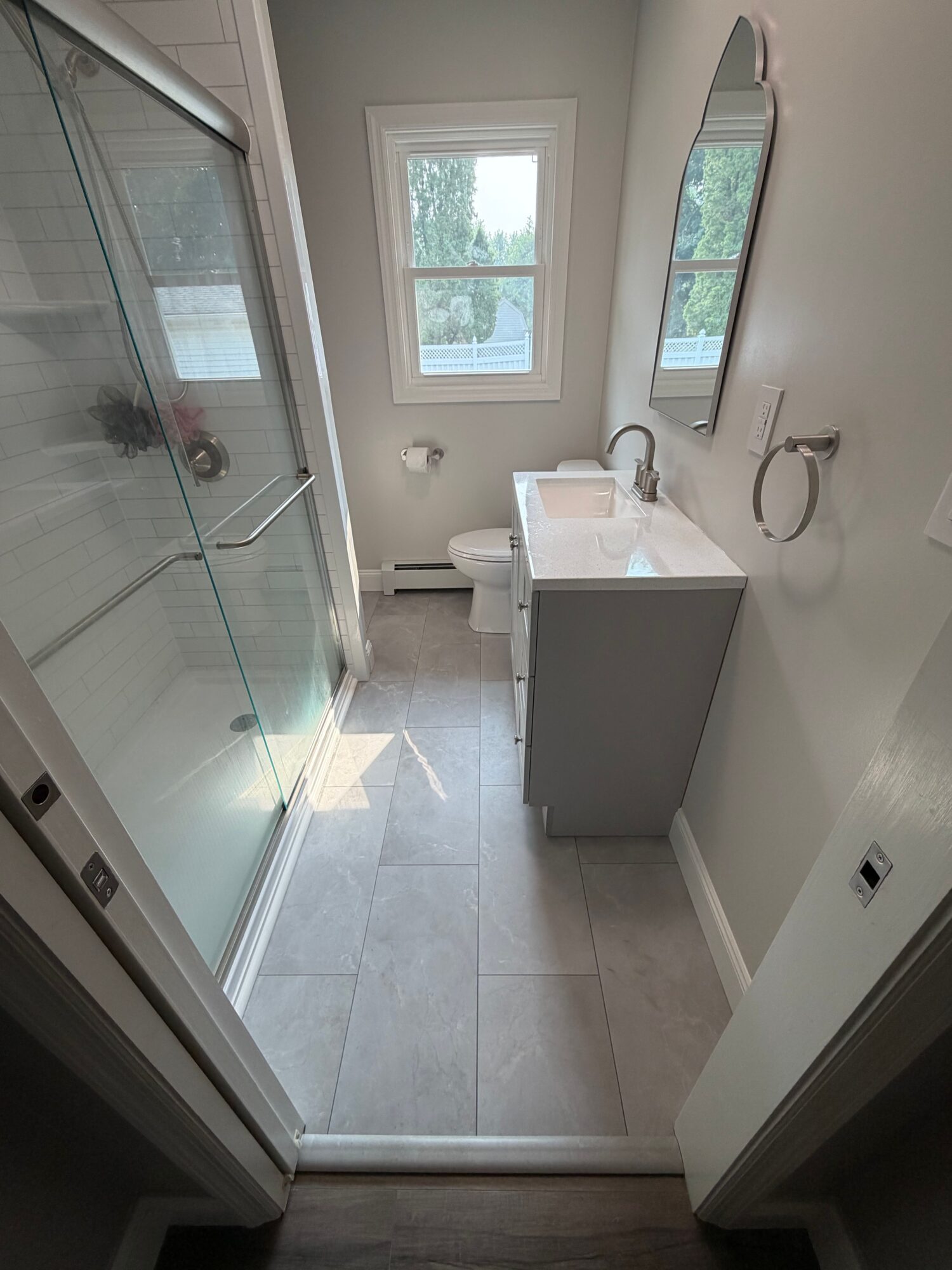 Bathroom with a window, sink, mirror, and tiled floor, viewed from the side with natural light coming in.