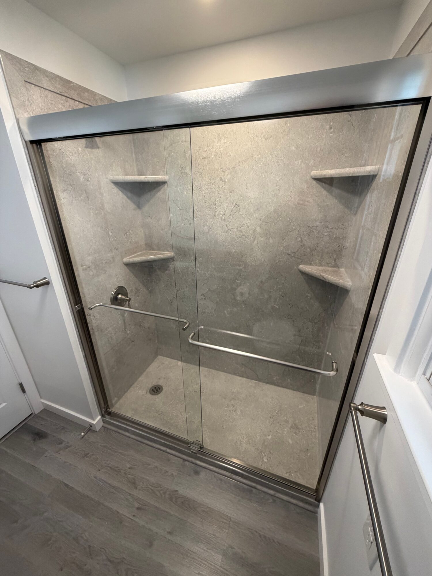 Glass shower enclosure with metal frame, showerhead, and built-in shelves, viewed from the side in a modern bathroom.
