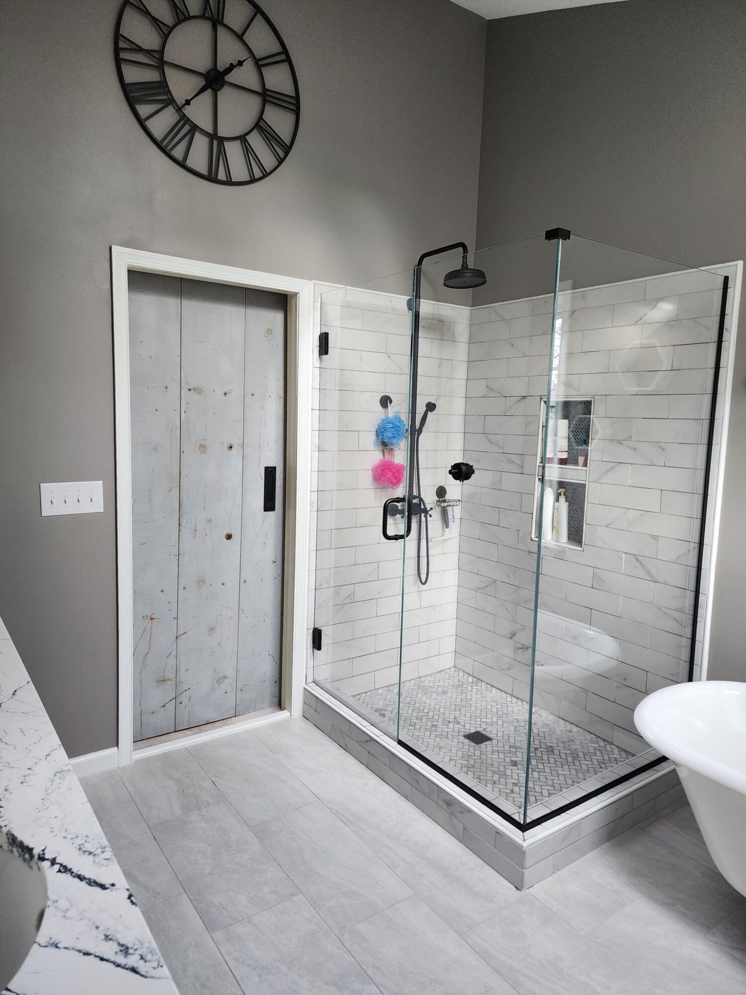 Bathroom with a glass shower enclosure, a wall clock, and a sliding door, with light gray walls and floor.