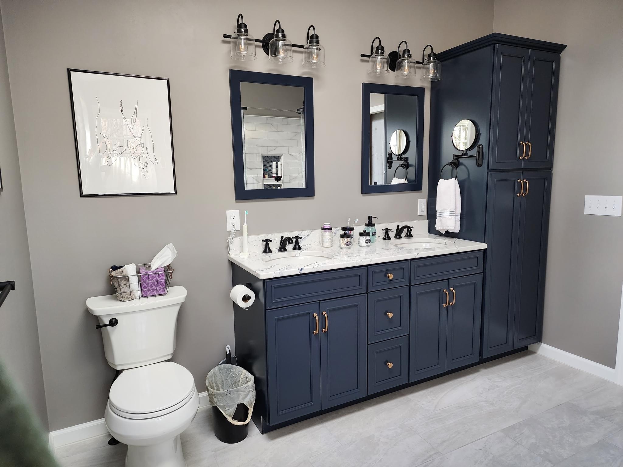 Bathroom with blue vanity, two mirrors, a toilet, and a tall cabinet, with gray walls and light-colored flooring.