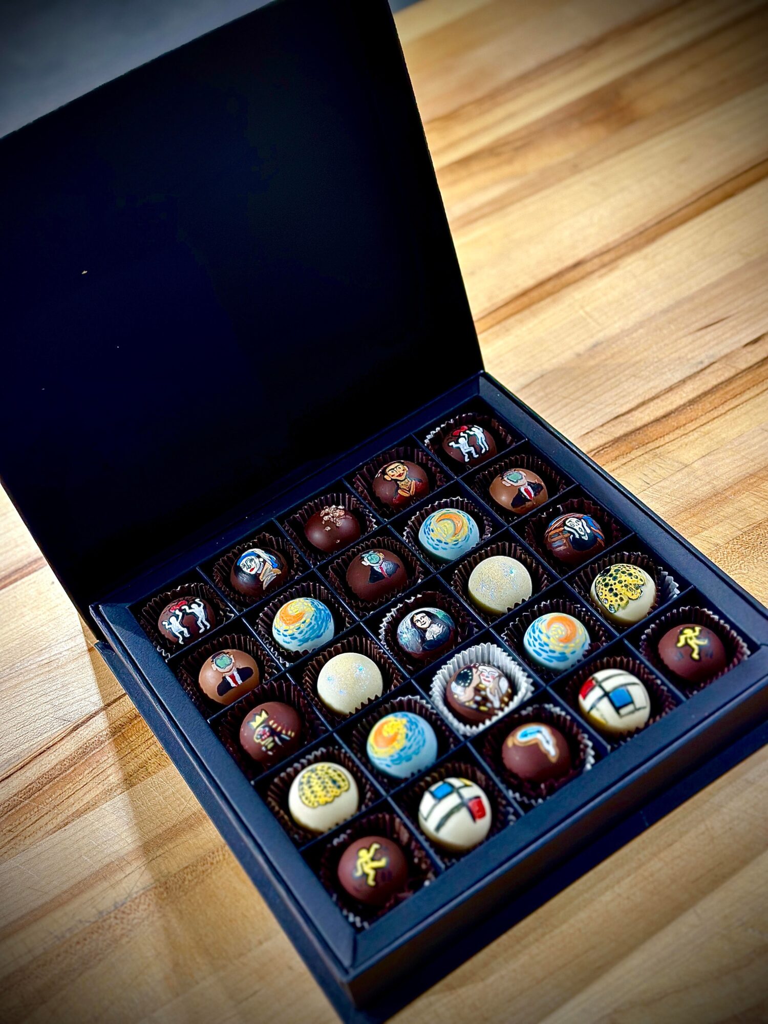 Open box of assorted chocolates on a wooden surface, showing various shapes and designs.
