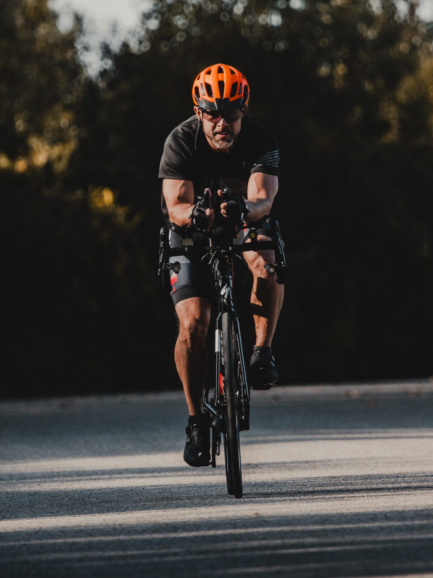 Cyclist wearing an orange helmet riding on a road with trees in the background.