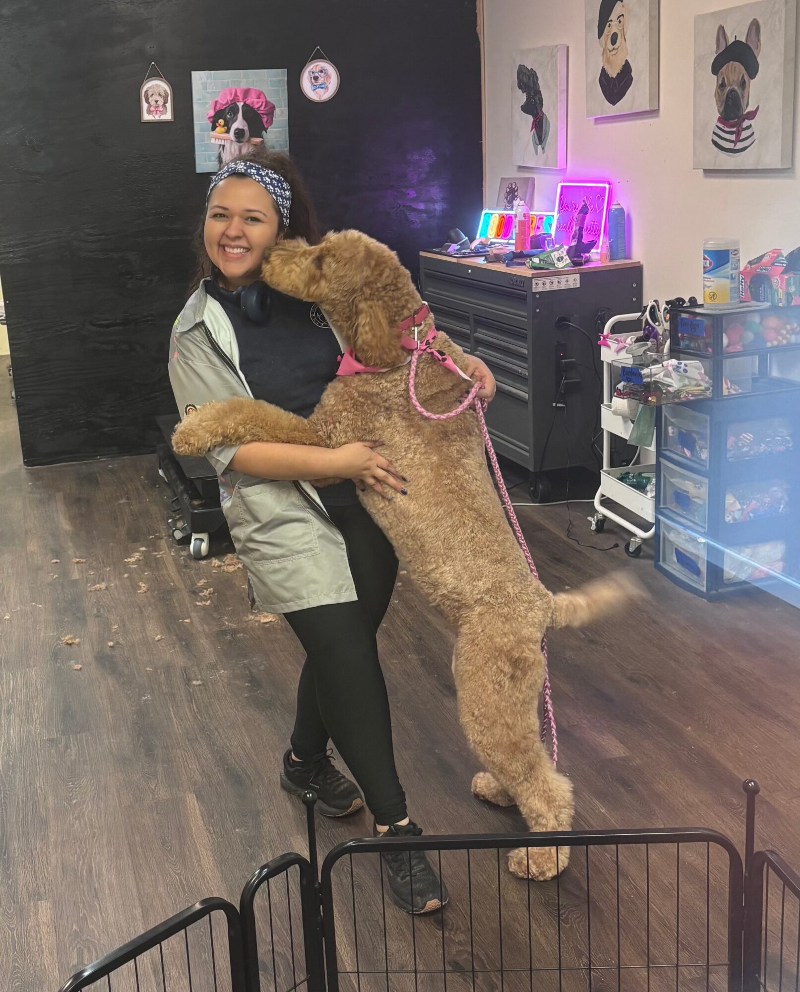 Woman smiling with a large dog hugging her, in an indoor space with colorful artwork and supplies in the background.