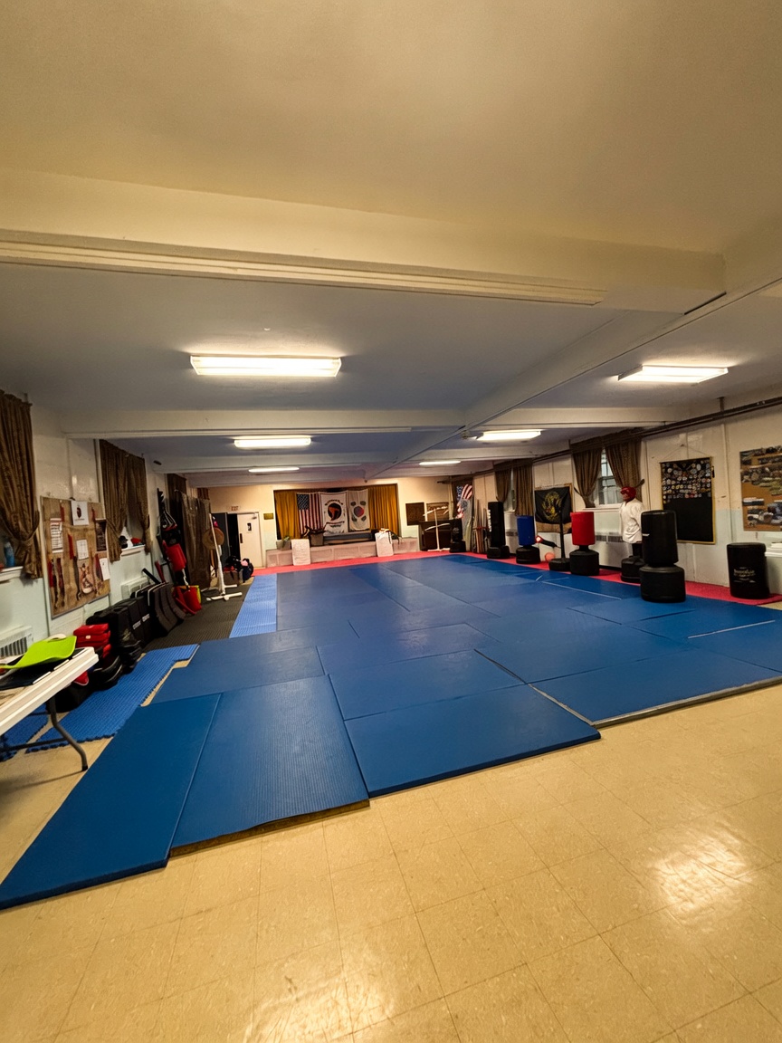 Indoor gym with blue mats covering the floor, walls decorated with posters, and equipment along the sides.