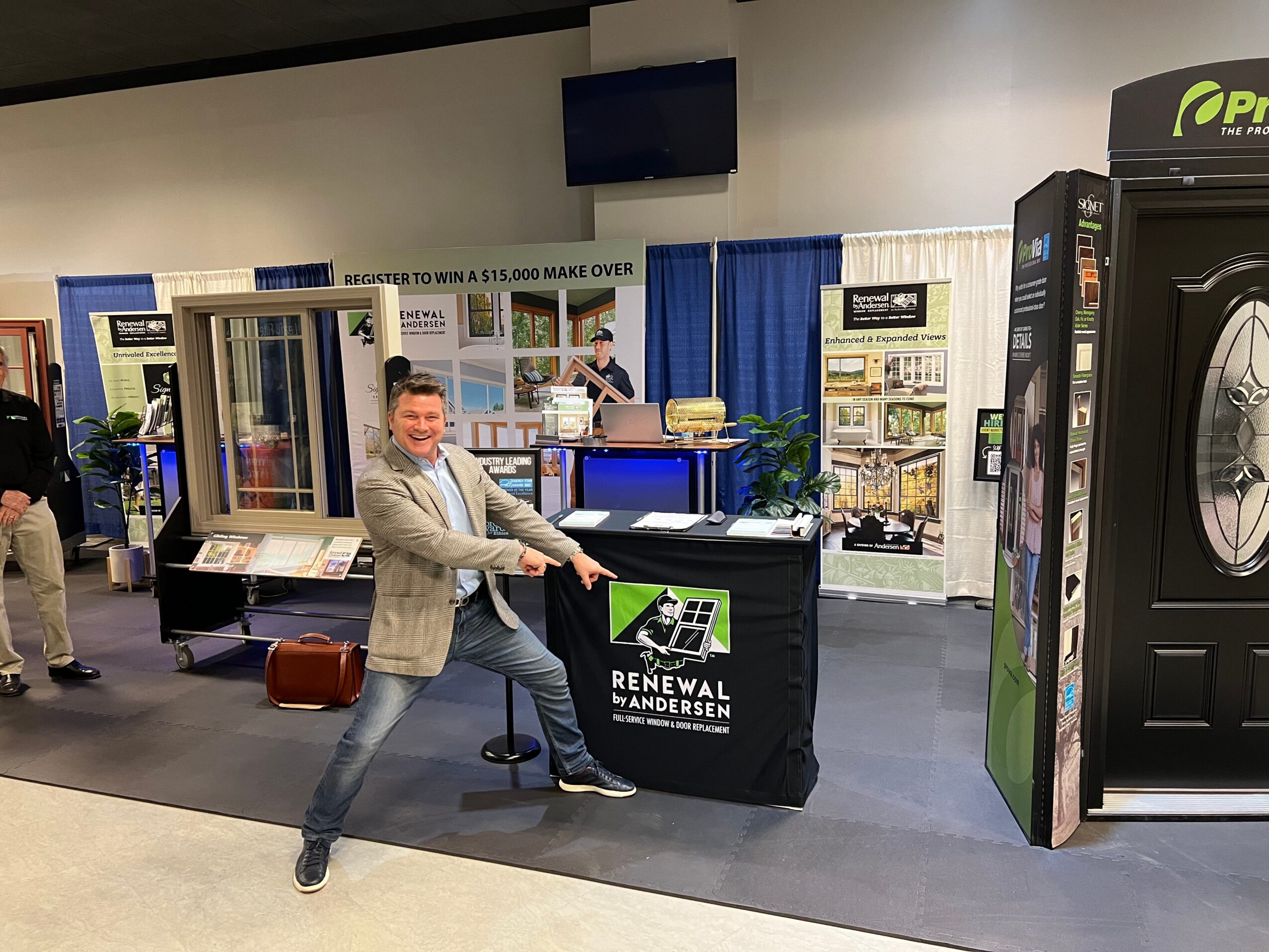 Person pointing at a booth with a black tablecloth and a green and white sign, in an indoor exhibition space.