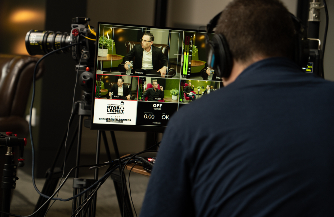Person wearing headphones monitors multiple video feeds on a screen during a recording session.