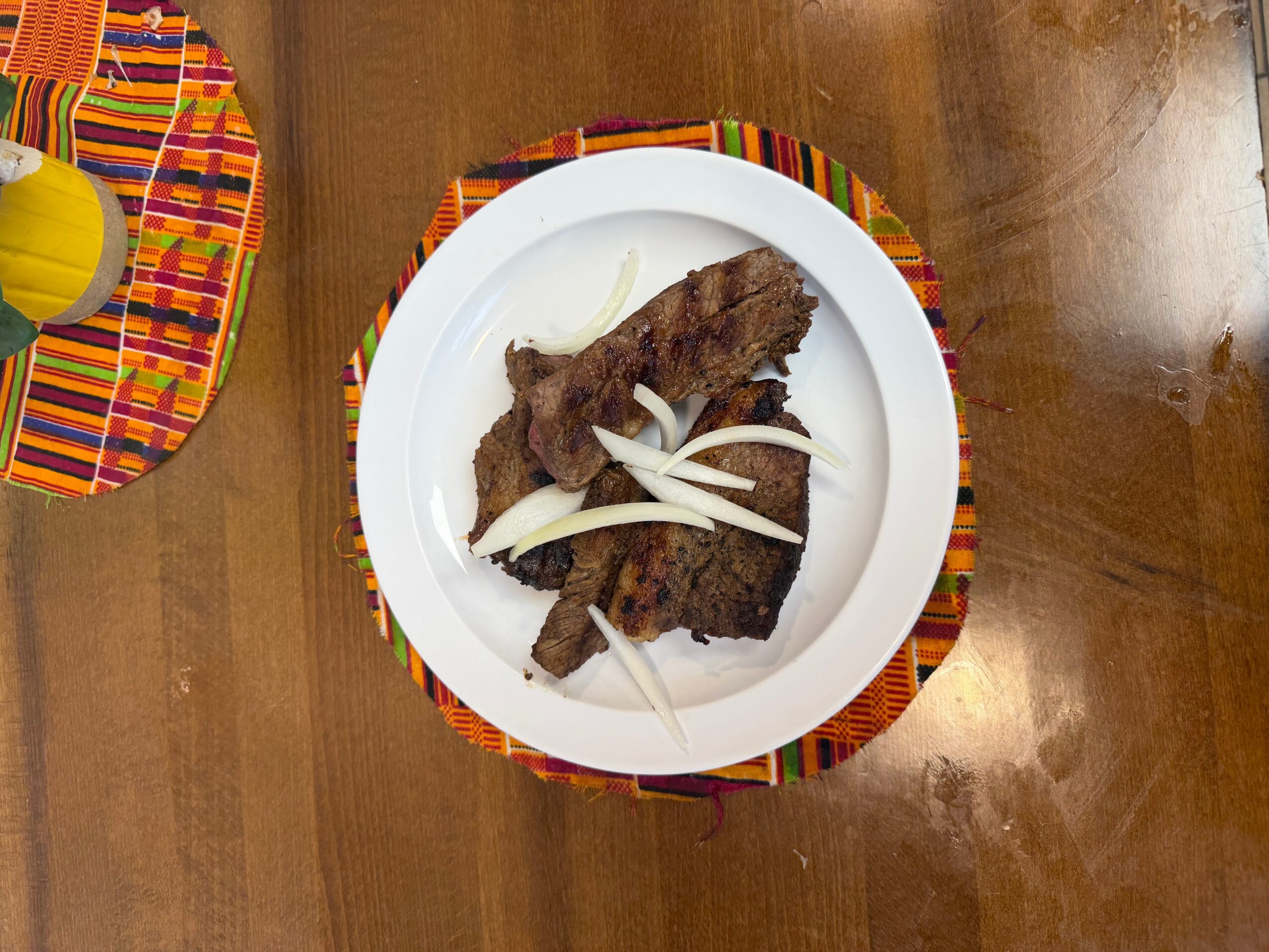 Plate with cooked meat and sliced onions on a colorful woven placemat, on a wooden table.