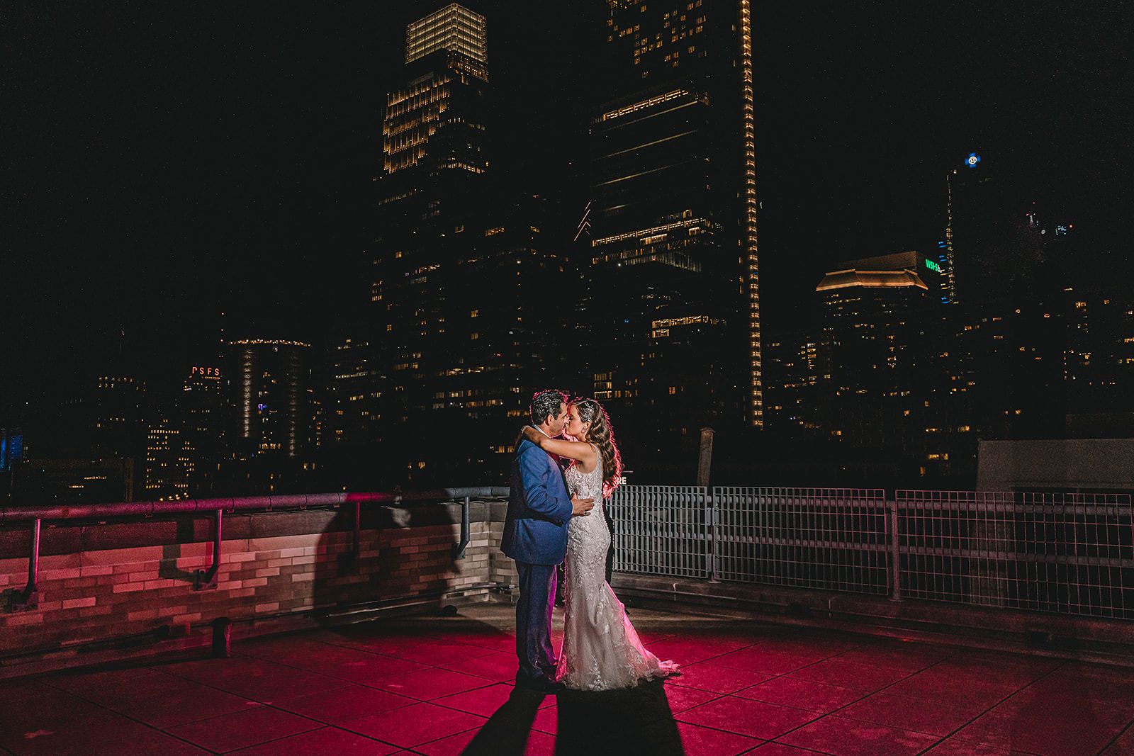 A couple dancing on a rooftop at night with a city skyline in the background, illuminated by tall buildings' lights.