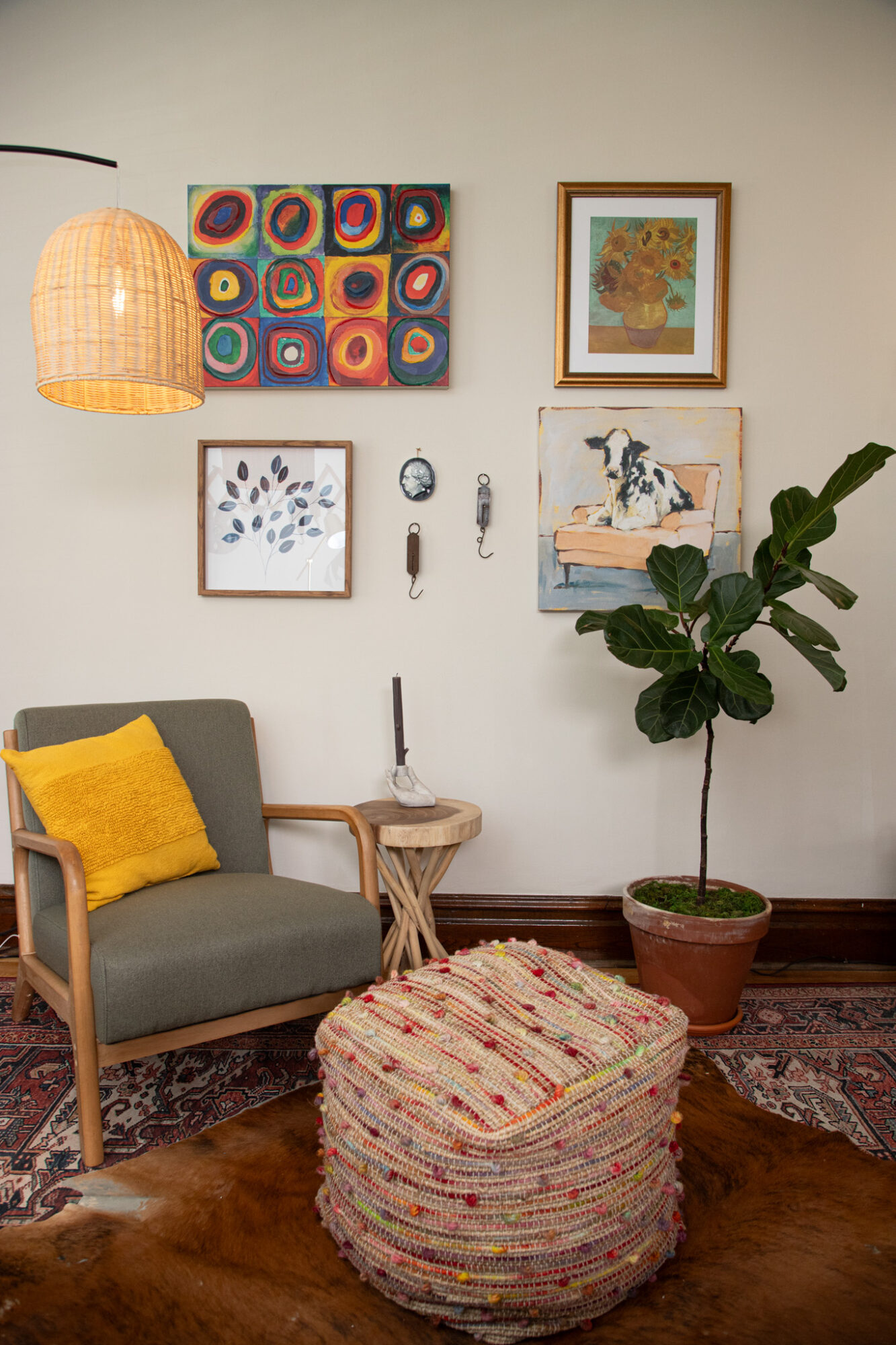 Living room with a gray sofa, yellow pillow, round woven ottoman, potted plant, wall art, and hanging lamp.