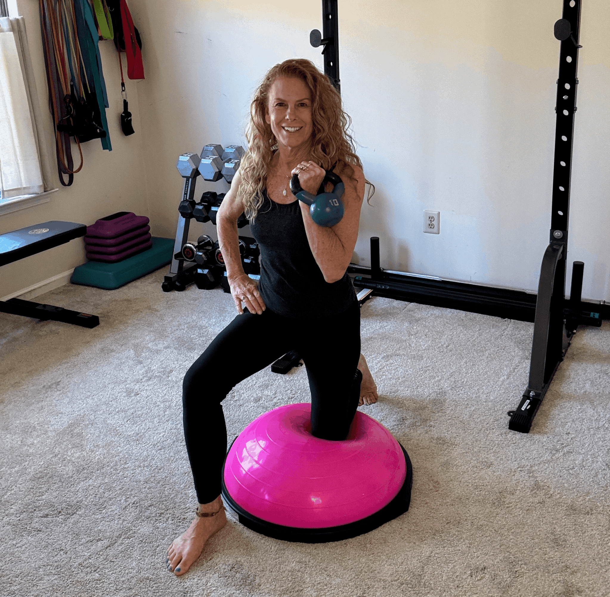 Woman with curly hair exercises with a kettlebell, kneeling on a pink balance disc in a home gym.