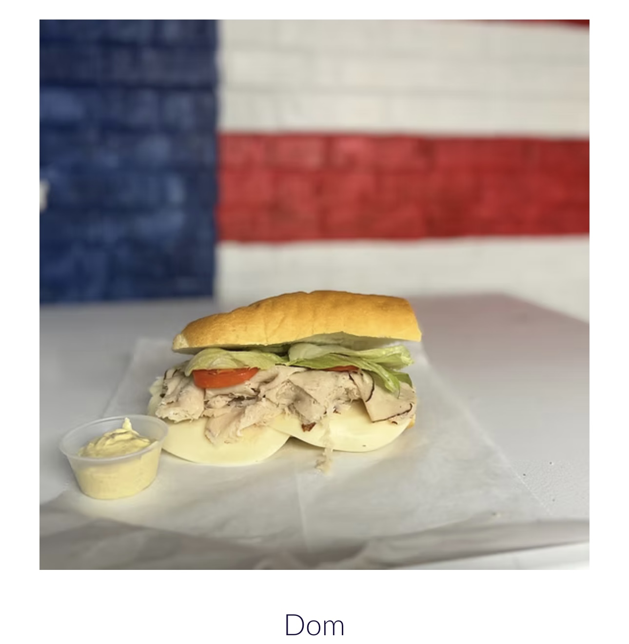 Sandwich with chicken, lettuce, tomato, and mayonnaise on a bun, with a small cup of mayonnaise on the side, against a red, white, and blue background.