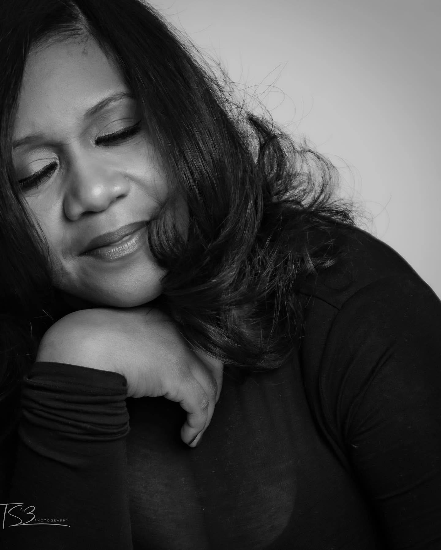Woman with closed eyes resting her head on her hand, smiling softly, black and white photo.