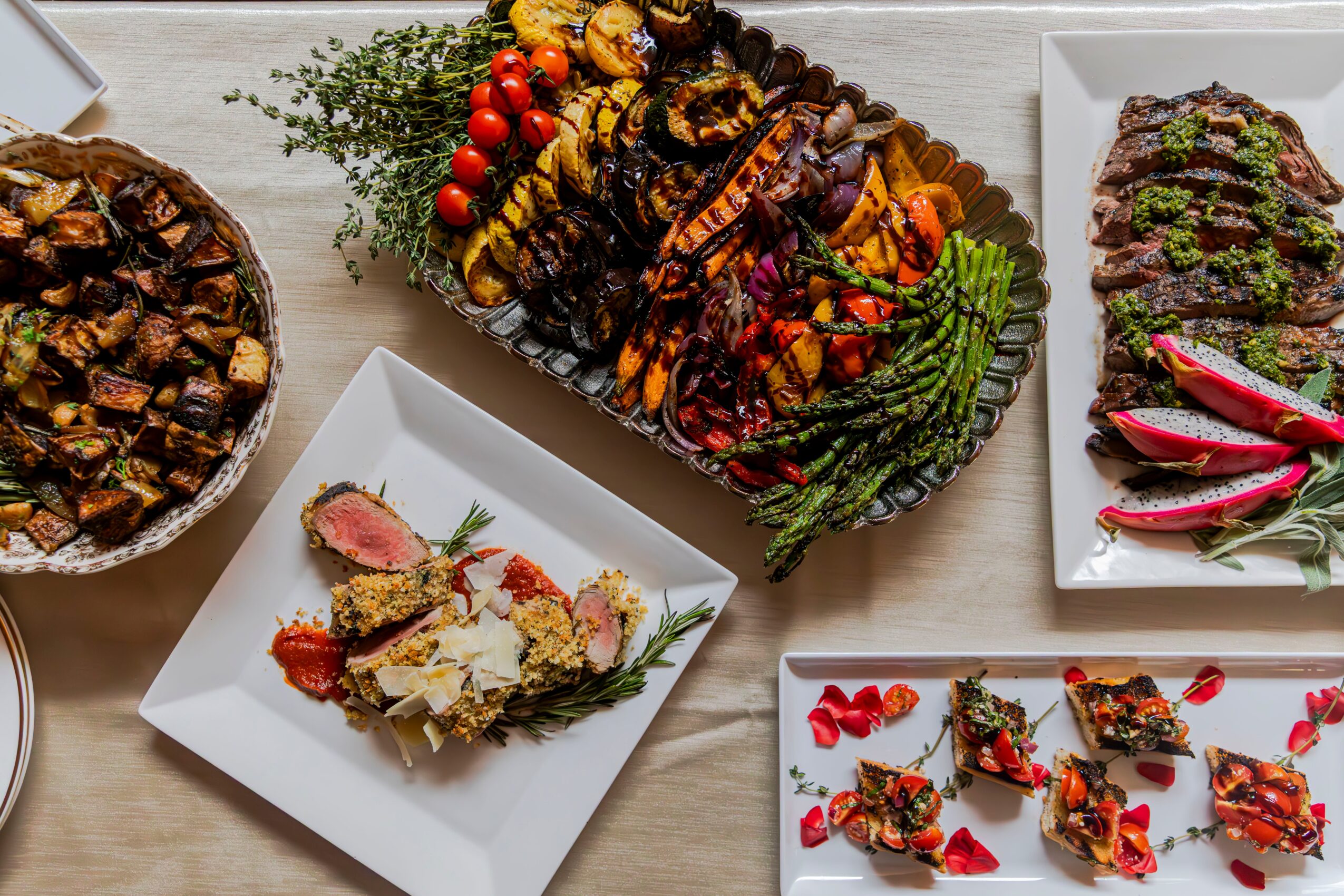 Assorted dishes including a vegetable platter, a salad with sliced meat, a roasted vegetable tray, and a plate of appetizers with toppings.