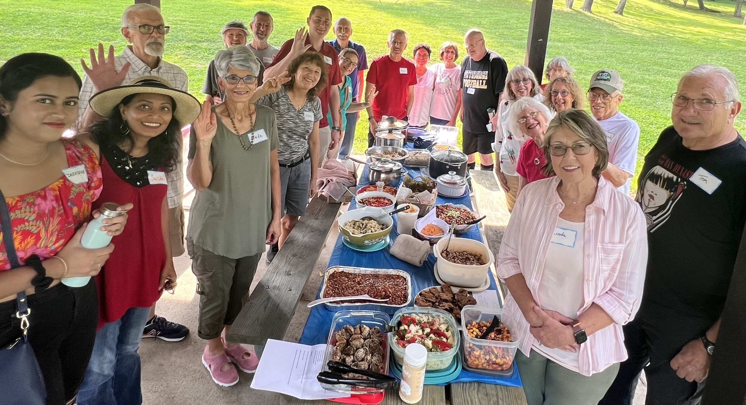 Group of people gathered around a table with food outdoors, smiling and posing for the photo.