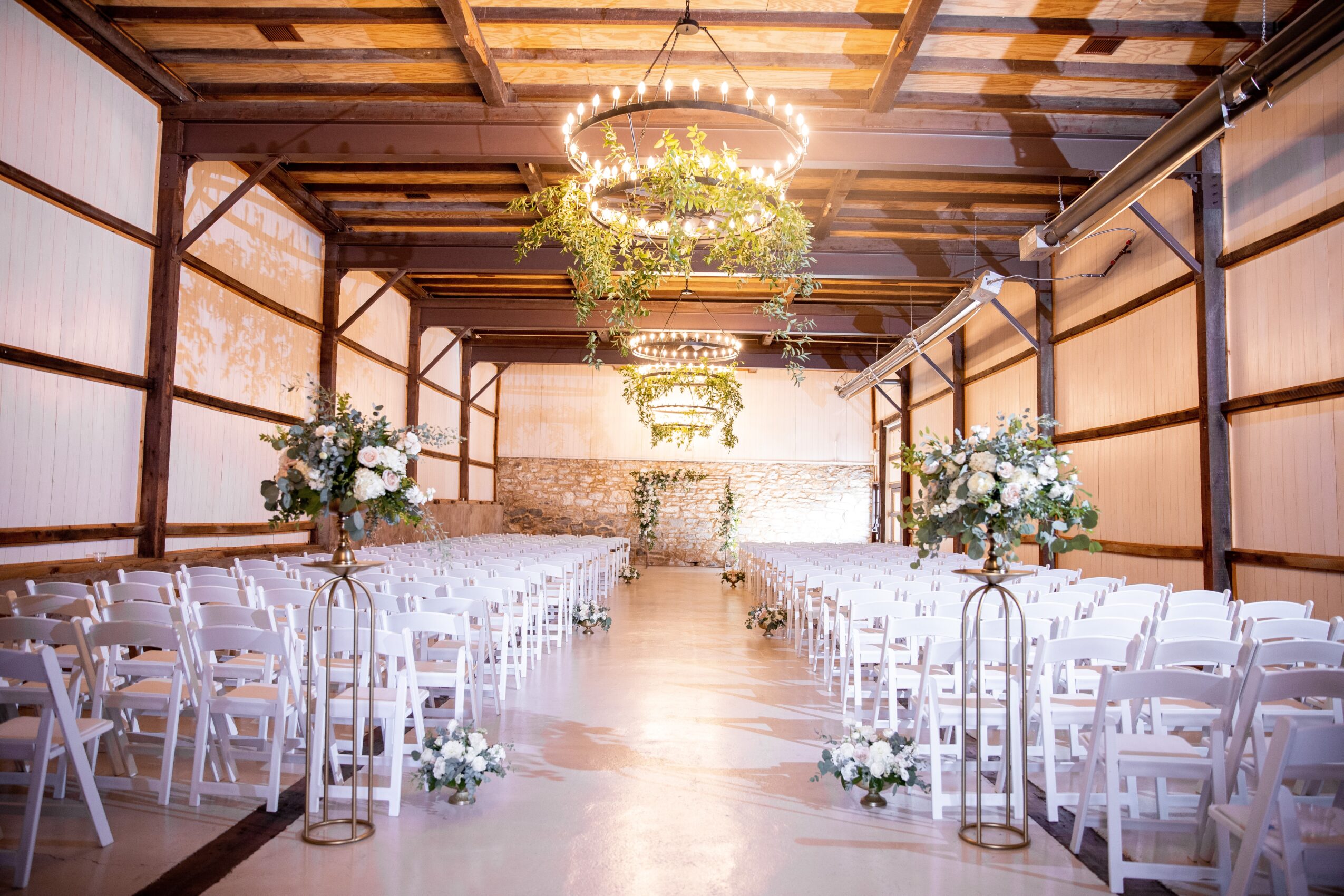 Indoor wedding venue with rows of white chairs, floral arrangements, and a chandelier, decorated for a ceremony.